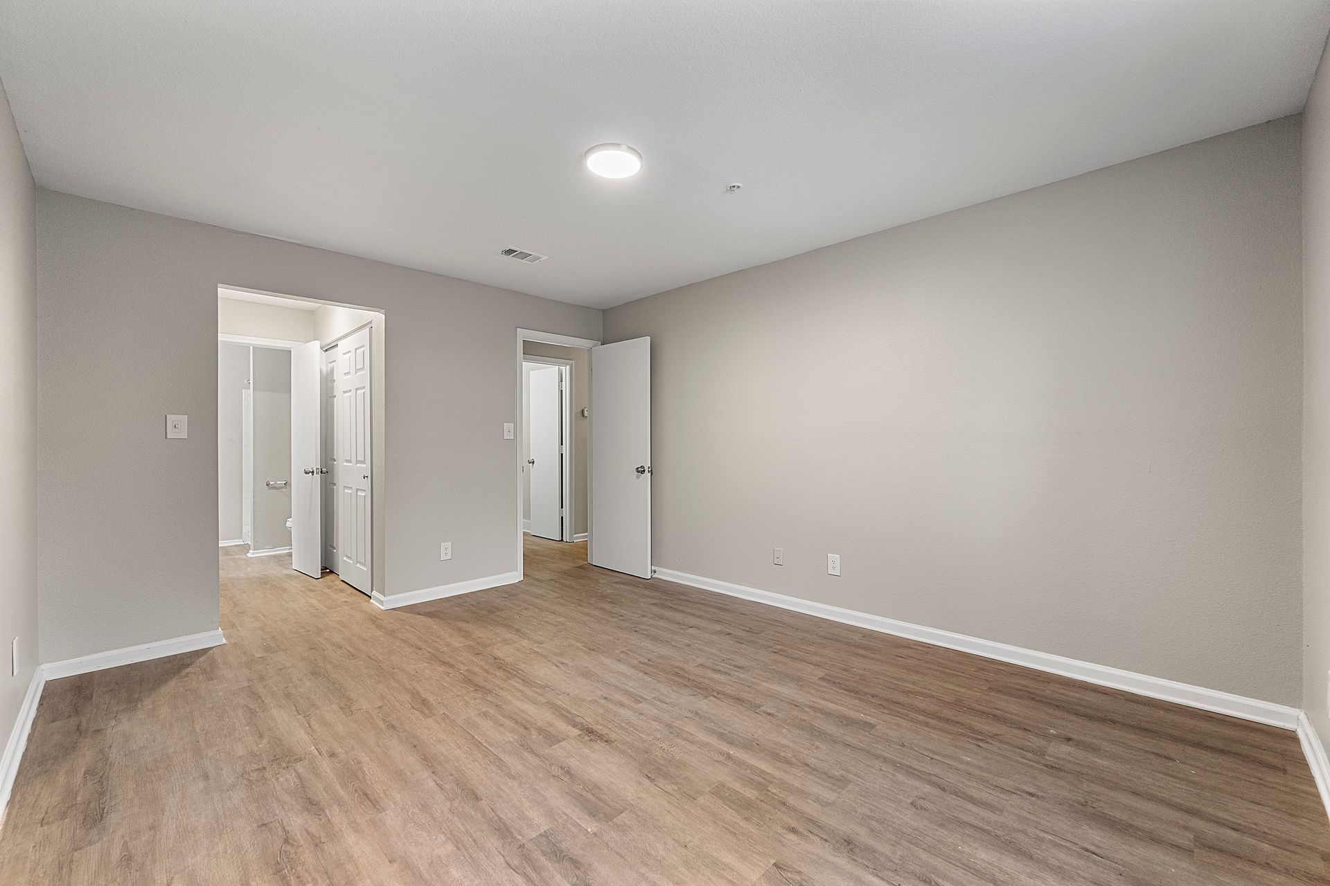 Empty modern bedroom with gray walls, white trim, and wood-look flooring