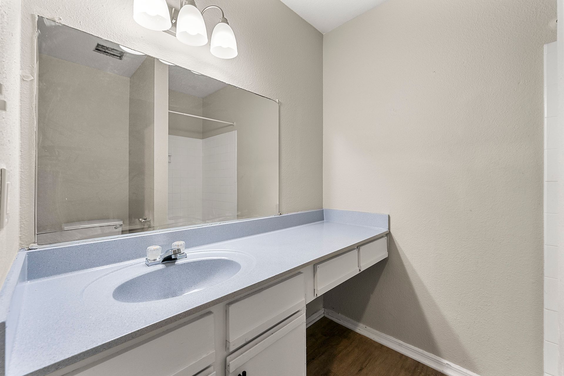 Empty bathroom vanity with large mirror, light blue countertop, and three-bulb overhead light.