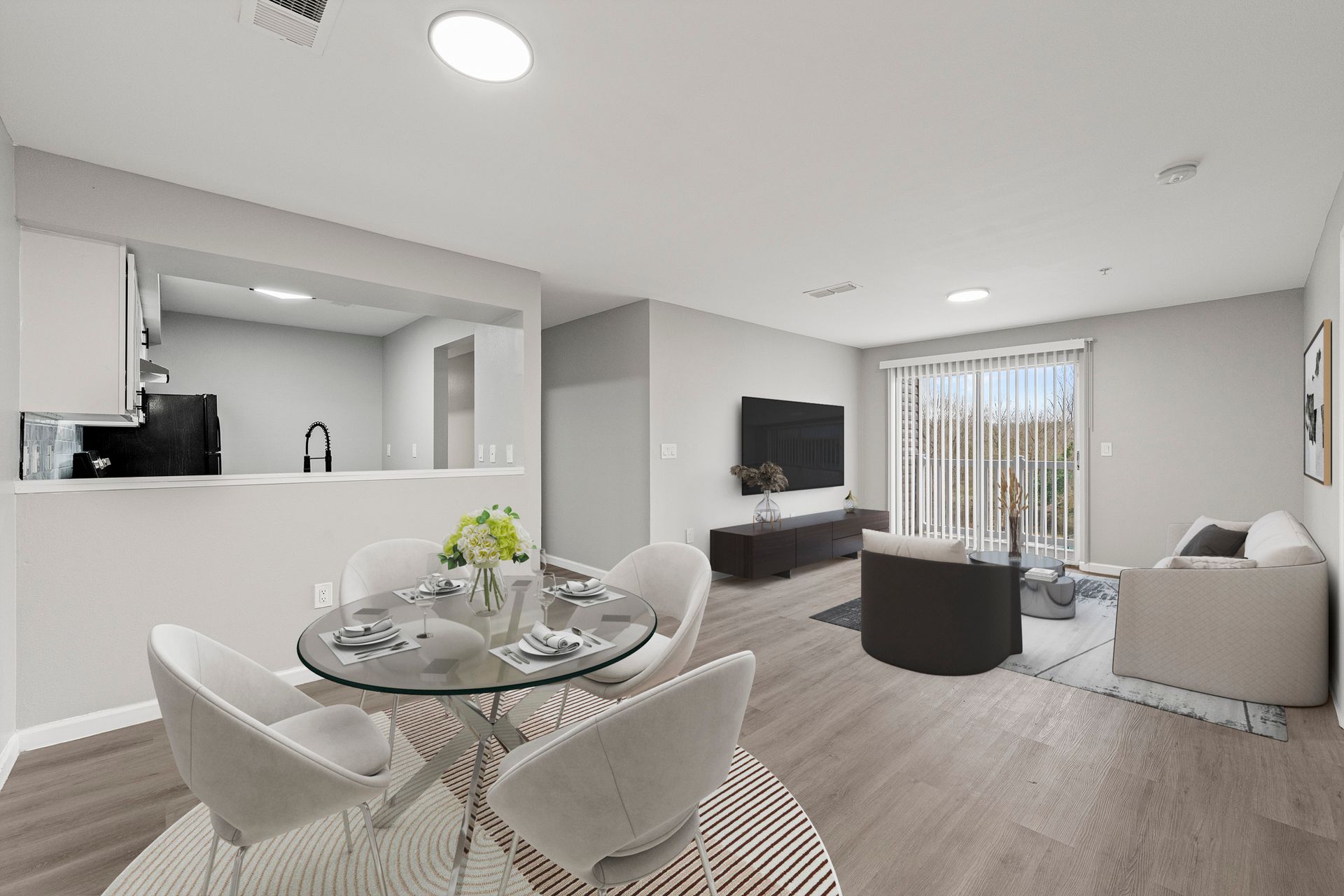 Bright open-plan living and dining room with gray furniture, wall-mounted TV, and kitchen pass-through.