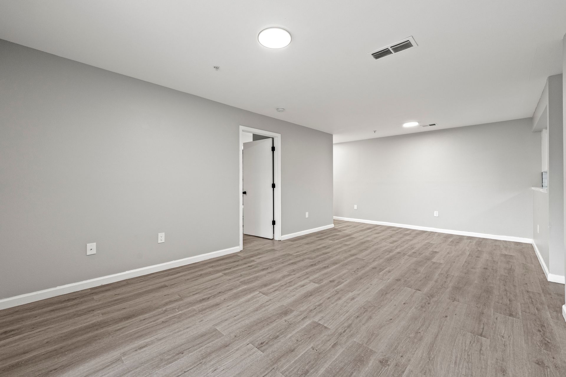 Empty modern room with gray walls, wood-look flooring, recessed lights, and a doorway opening to a hall