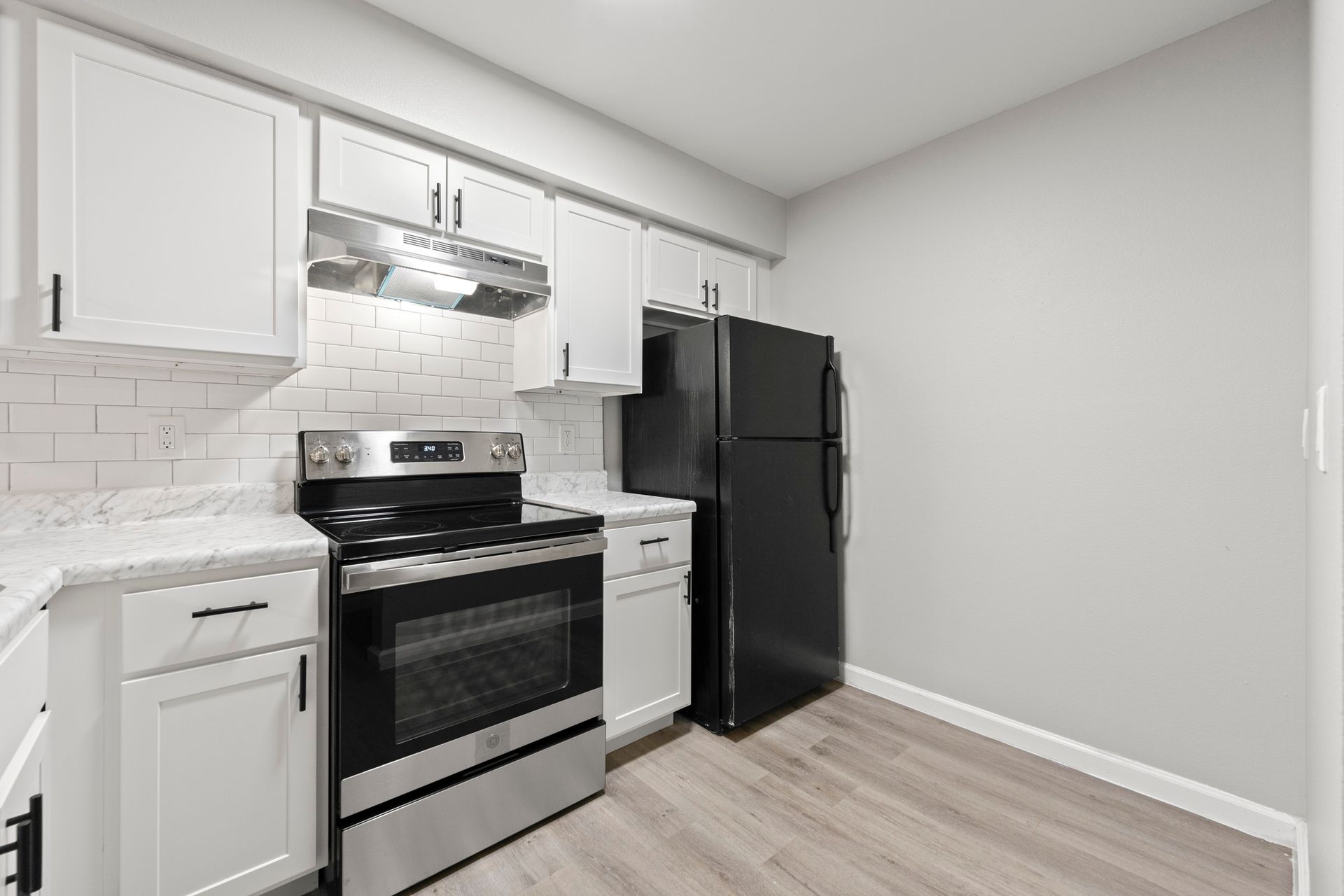 Small modern kitchen with white cabinets, stainless steel stove, and black refrigerator