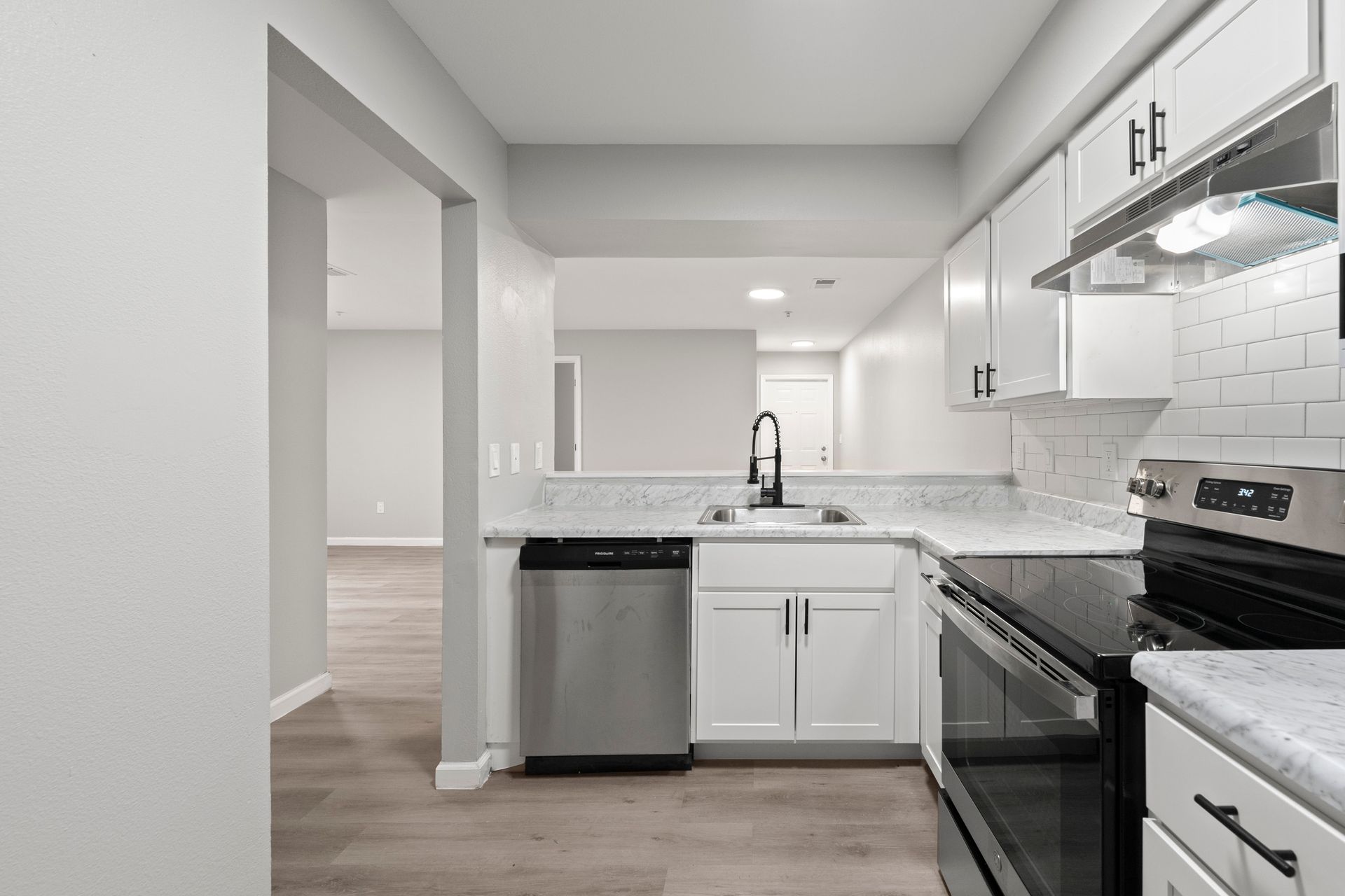 Modern white kitchen with stainless steel appliances, marble countertops, and a doorway to an adjacent room