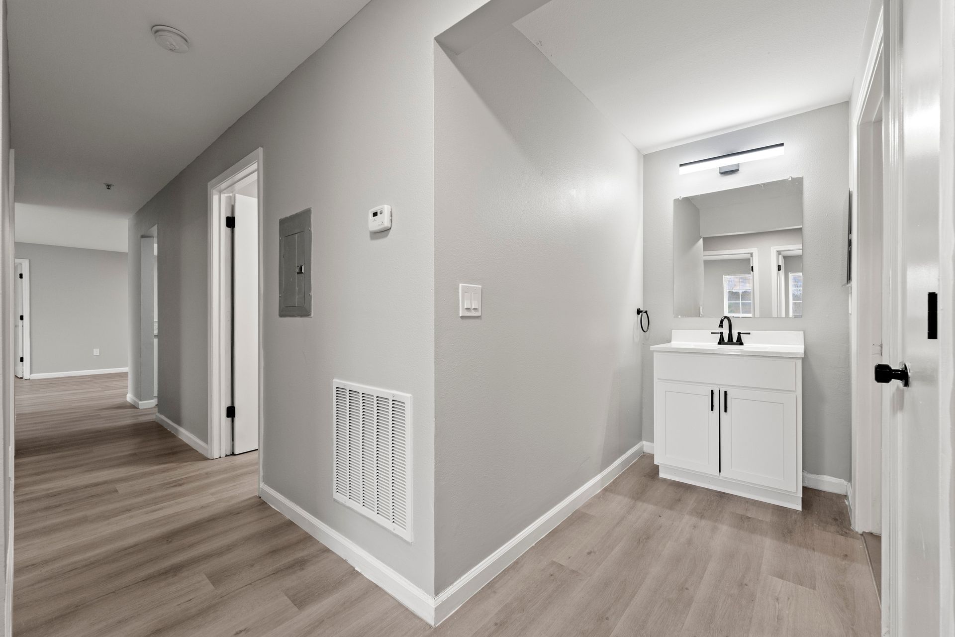 Bright hallway with wood floors, gray walls, and a small vanity sink alcove on the right.