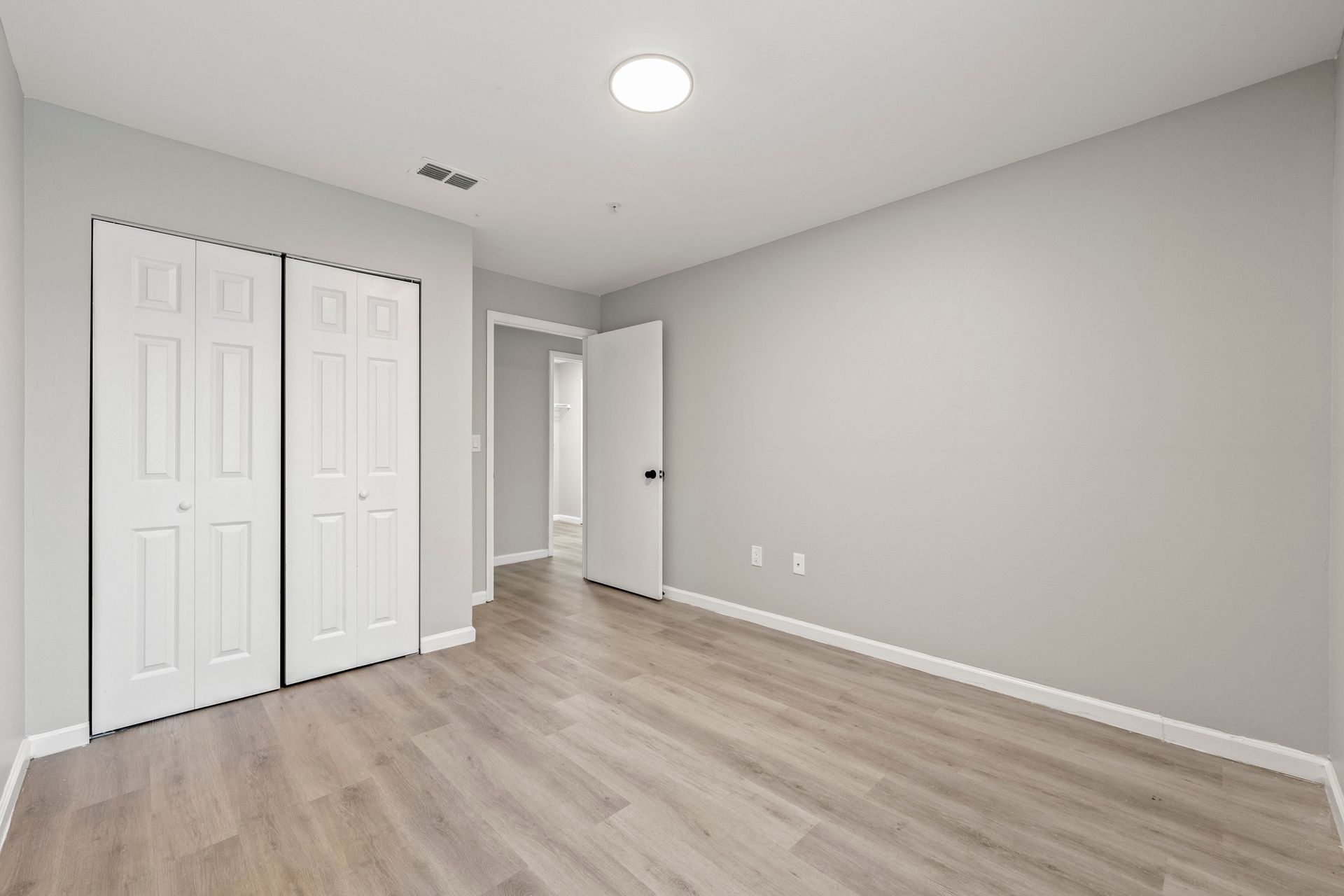 Empty gray bedroom with white closet doors, wood floors, and a doorway to the hall