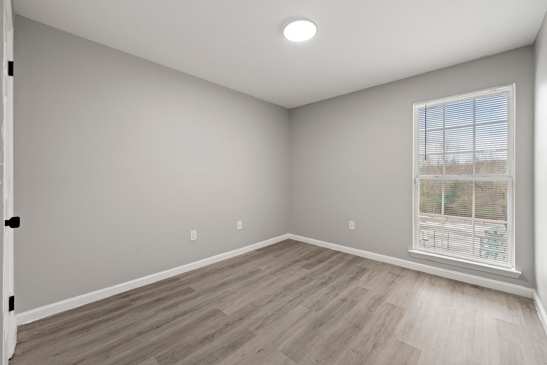 Empty gray bedroom with wood floors, white trim, and a window letting in daylight