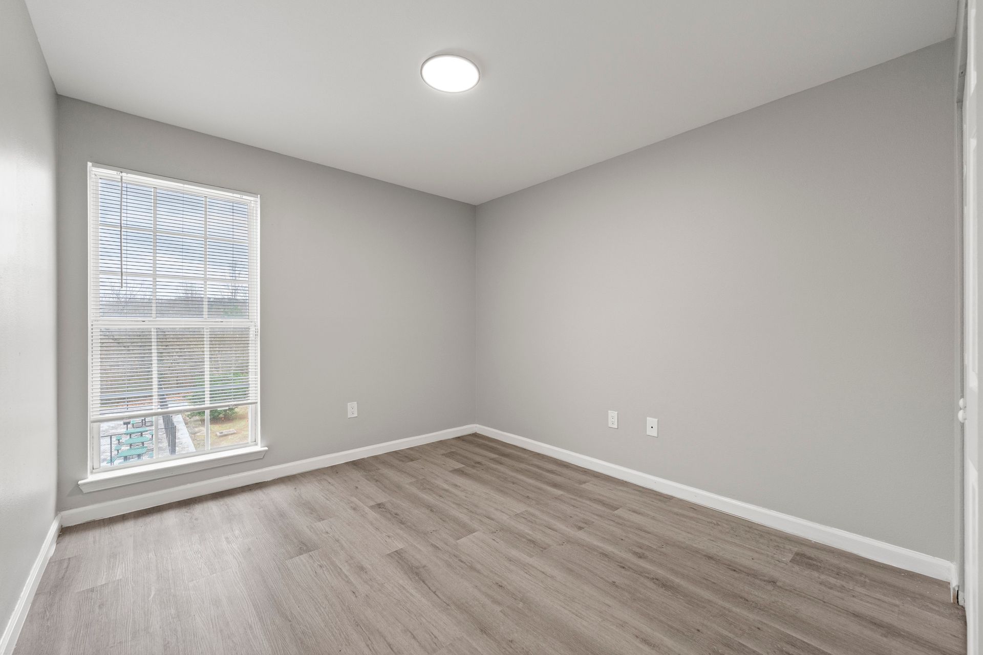 Empty gray bedroom with wood flooring and a window