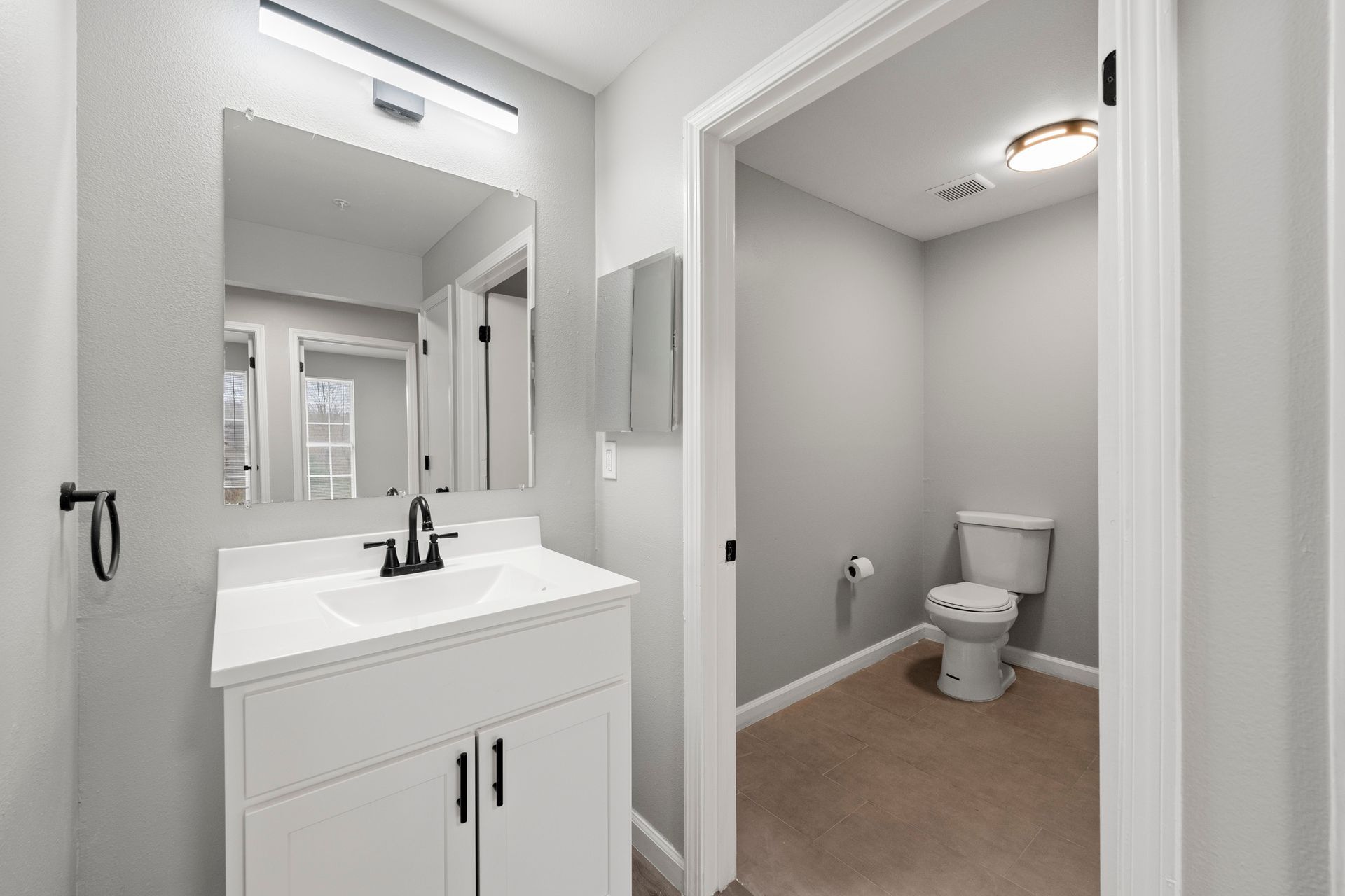 Bright bathroom with white vanity, large mirror, and a toilet in a separate alcove.