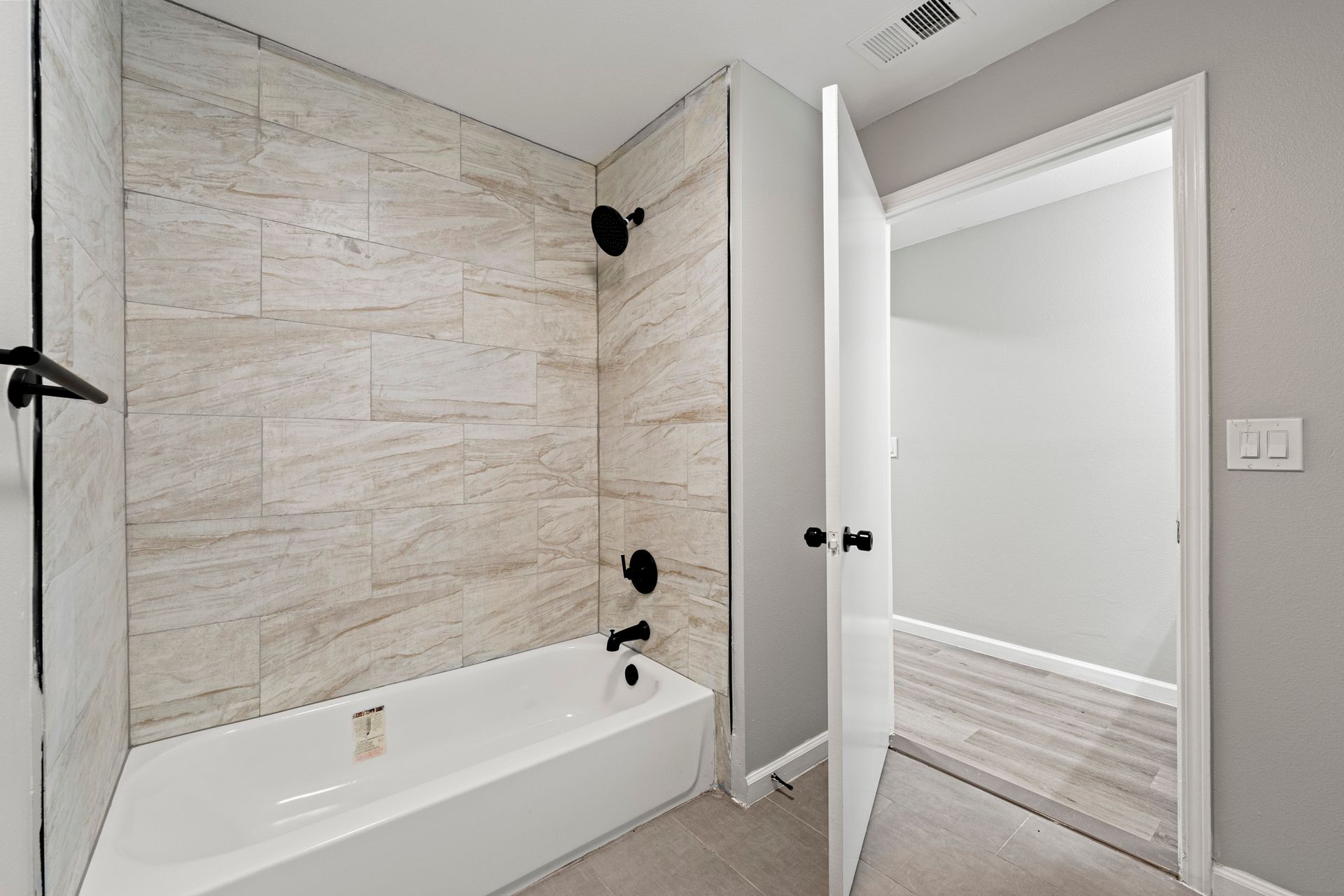 Modern white bathroom with tub, tiled shower walls, and open door to a hallway