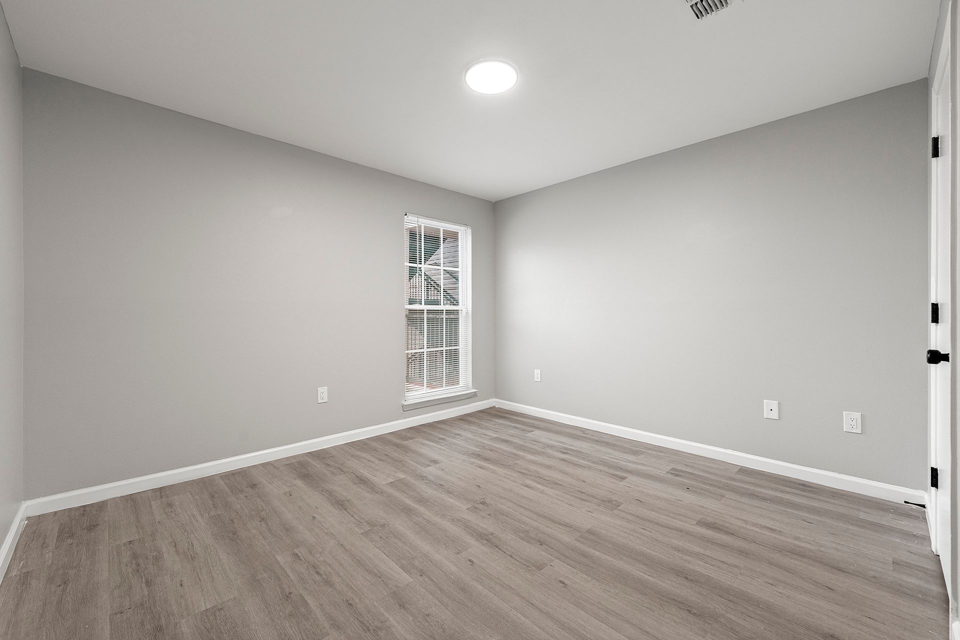 Empty gray bedroom with wood-look flooring and a small window near the corner.