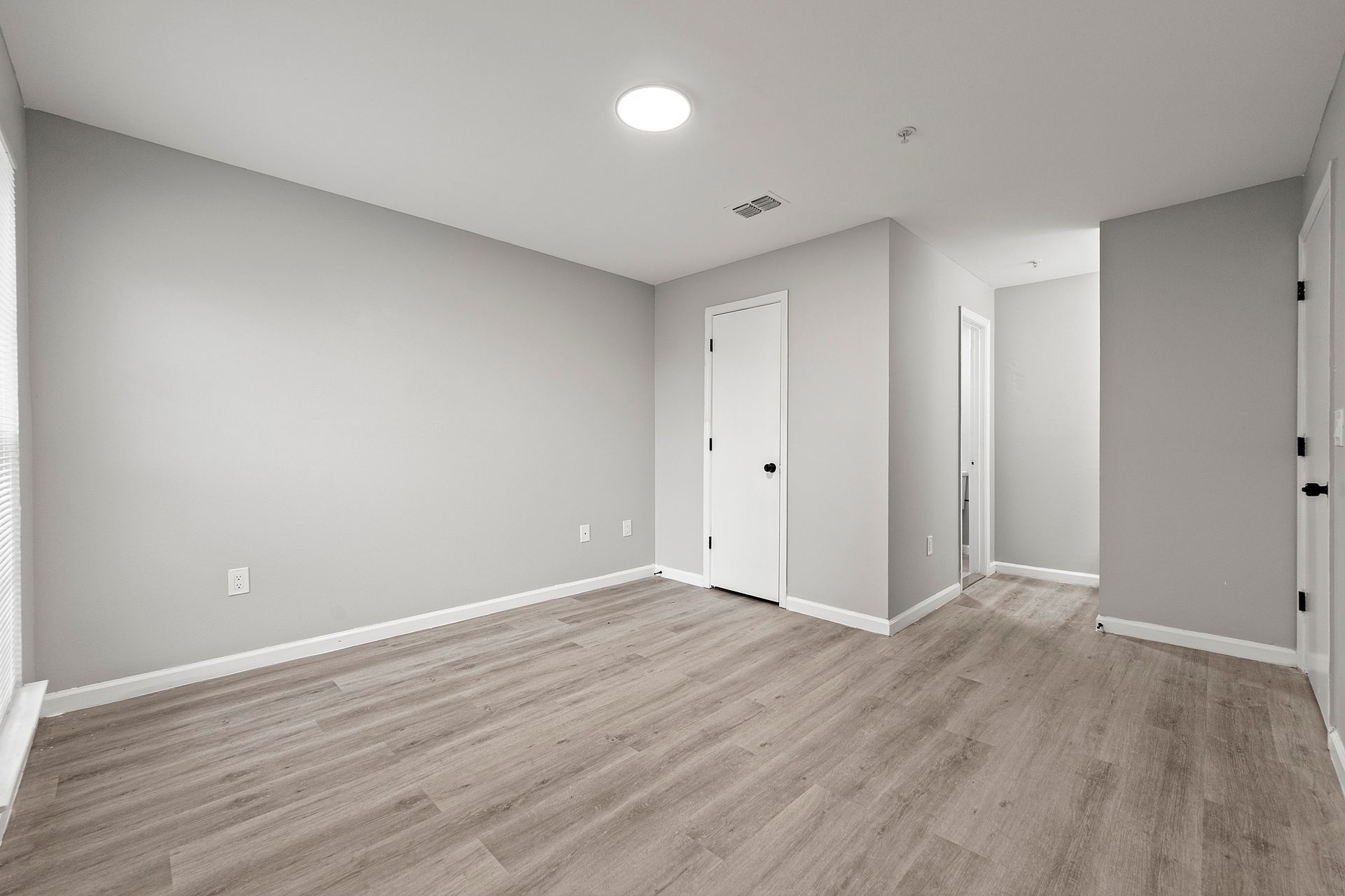 Empty gray bedroom with wood flooring, white doors, and recessed ceiling light.