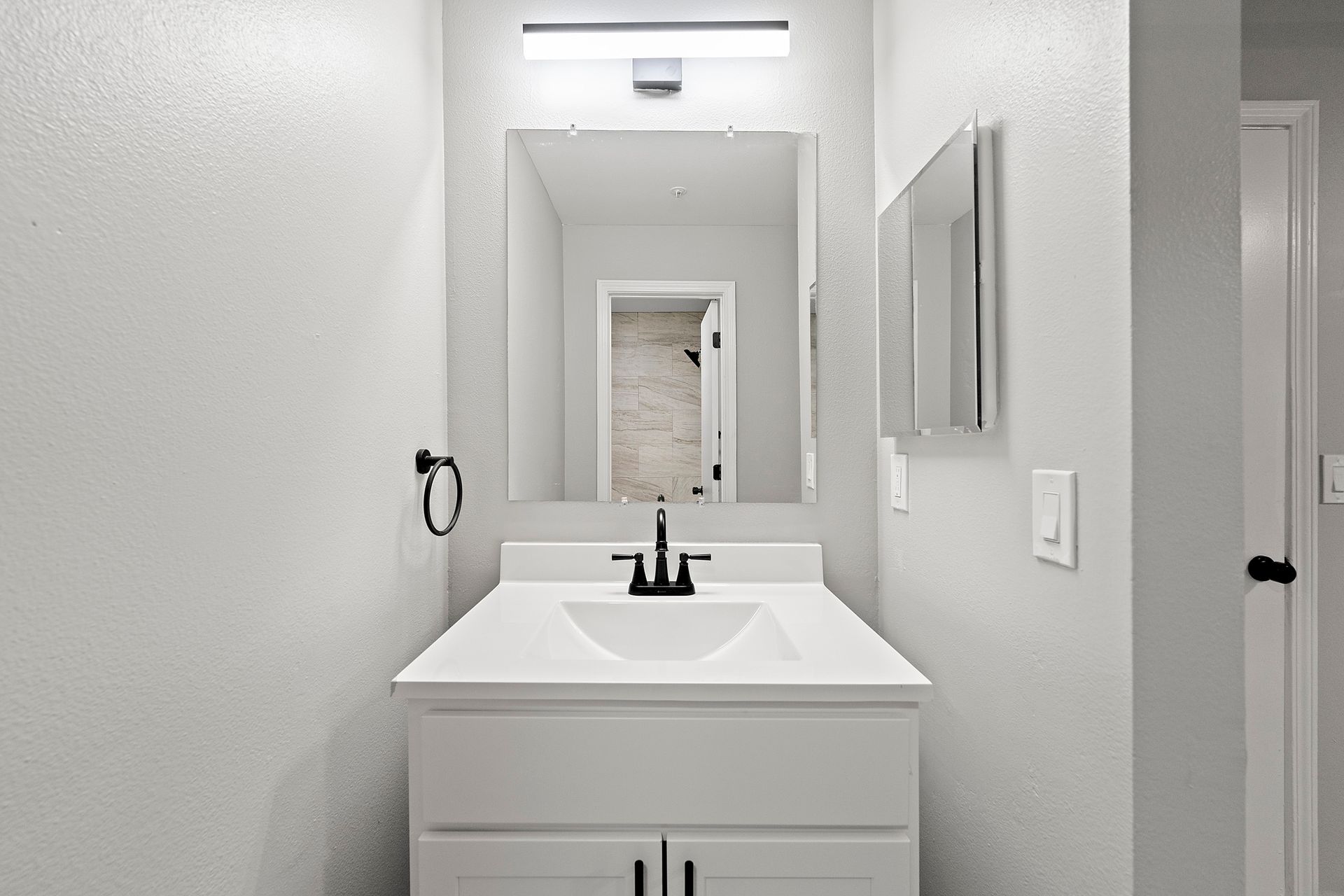 Bright bathroom vanity with white sink, black faucet, mirror, and gray walls.