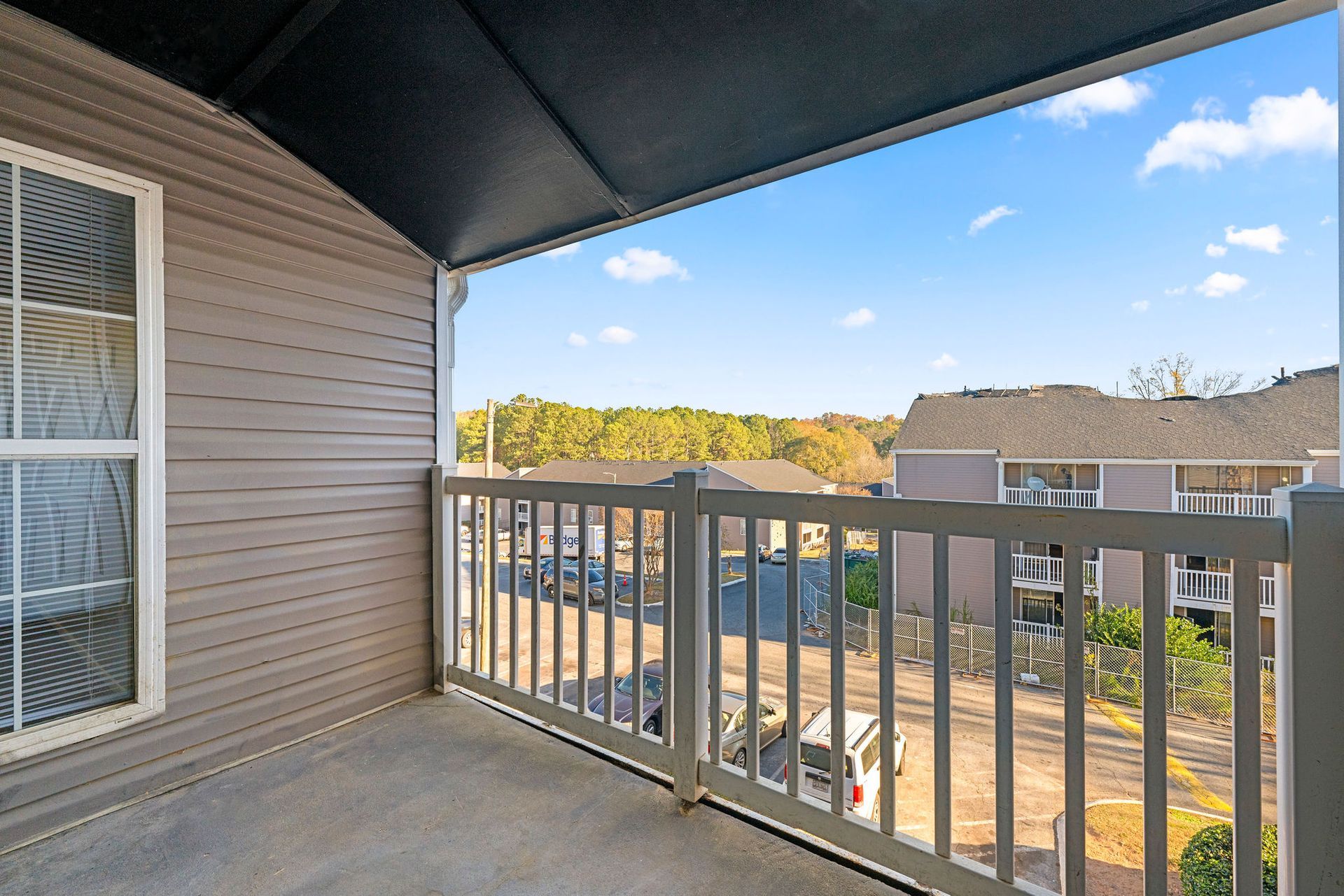 Balcony view with white railing overlooking apartment buildings and trees under a blue sky