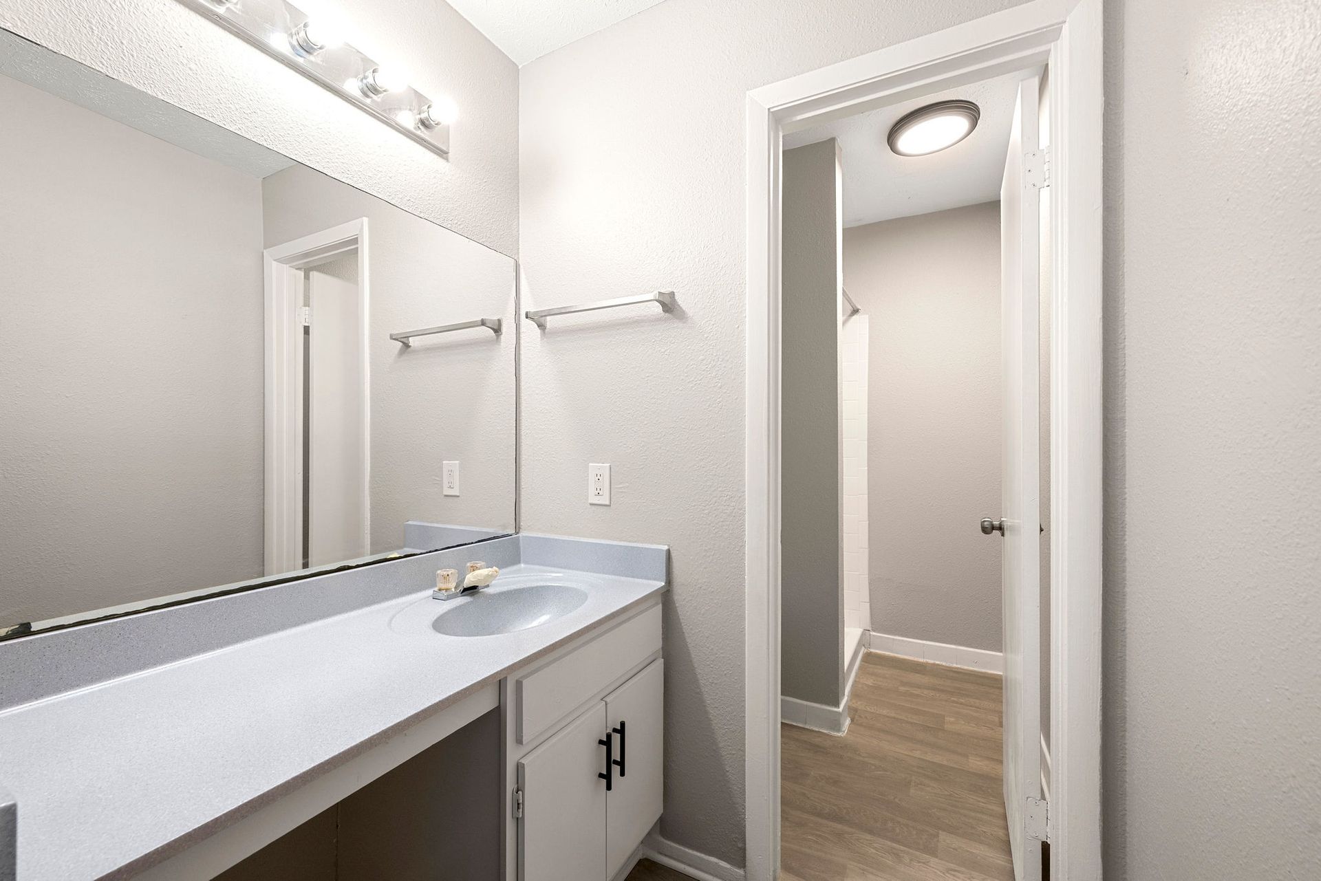 Bright white bathroom vanity with mirror, sink, and doorway to a hallway with wood flooring
