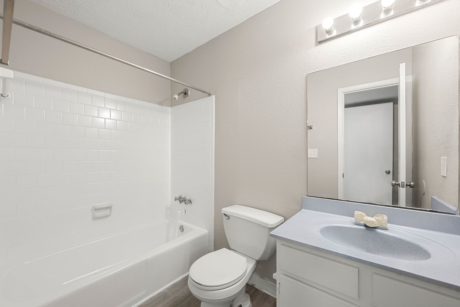 Bright bathroom with white tub, toilet, vanity, and large mirror under lights.