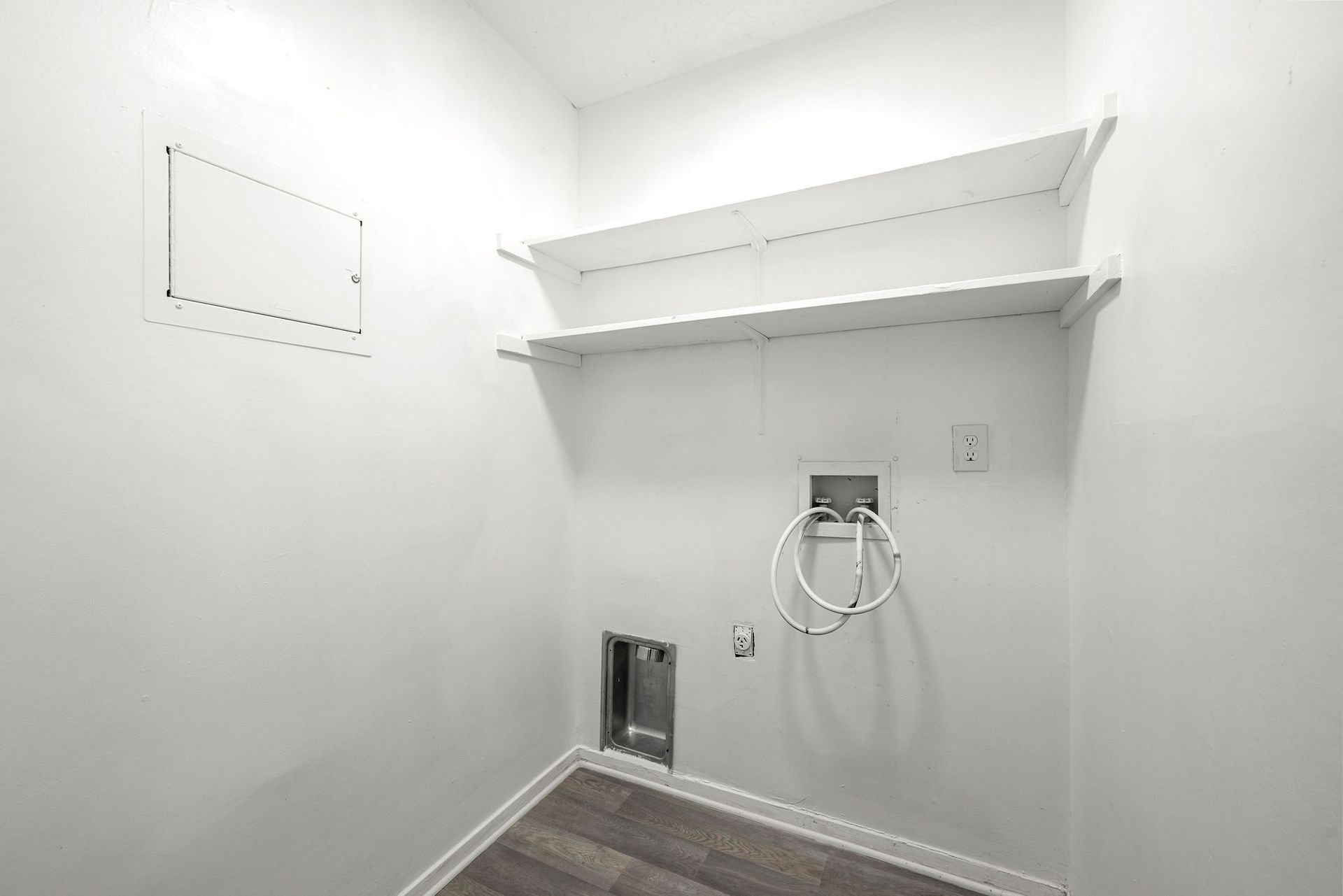 Small white utility closet with wall shelves, a hose hookup, and a floor drain.