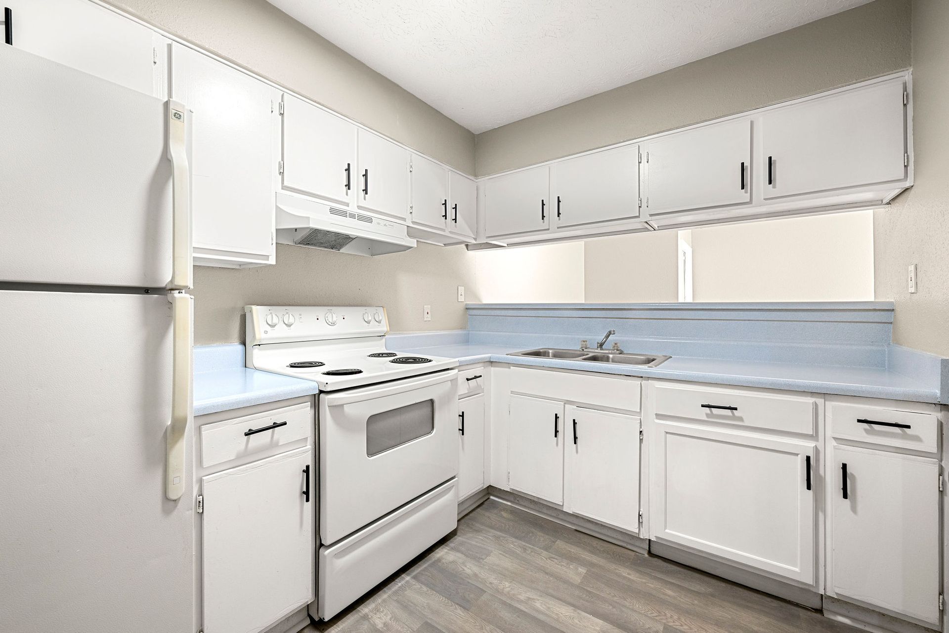 Bright white kitchen with stove, refrigerator, and L-shaped cabinets with blue backsplash.