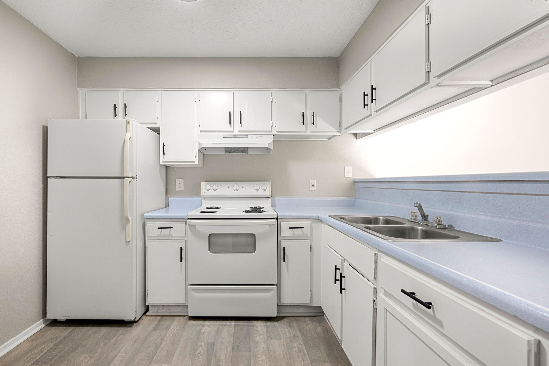 Bright white galley kitchen with fridge, stove, cabinets, and blue backsplash countertops