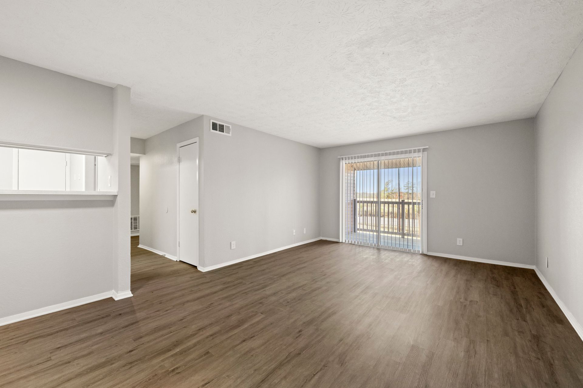 Empty modern living room with gray walls, wood-look floors, and a sliding glass door to a balcony.