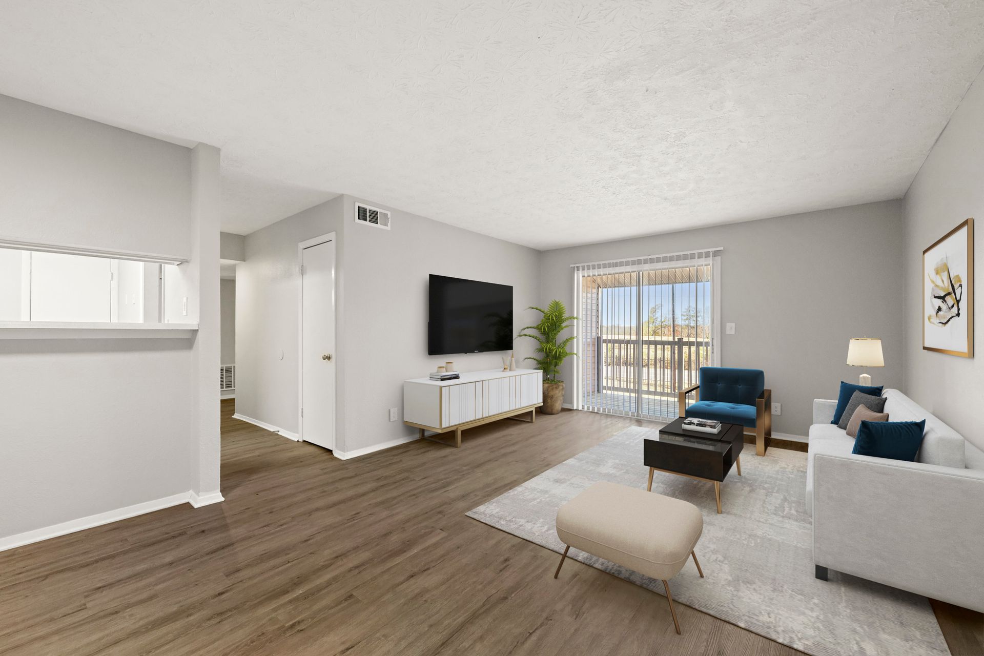 Bright modern living room with TV, gray sofa, blue chairs, and wood flooring, opening to a balcony.