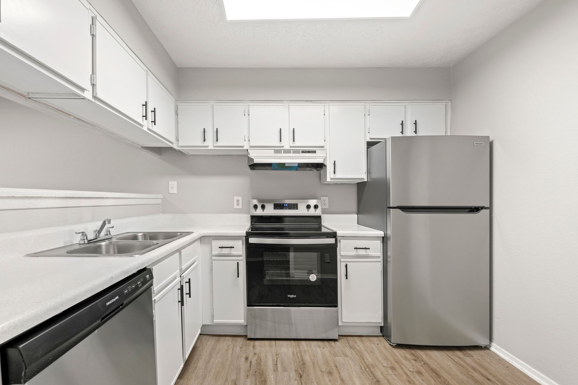 Bright white kitchen with stainless steel appliances, white cabinets, and light wood flooring
