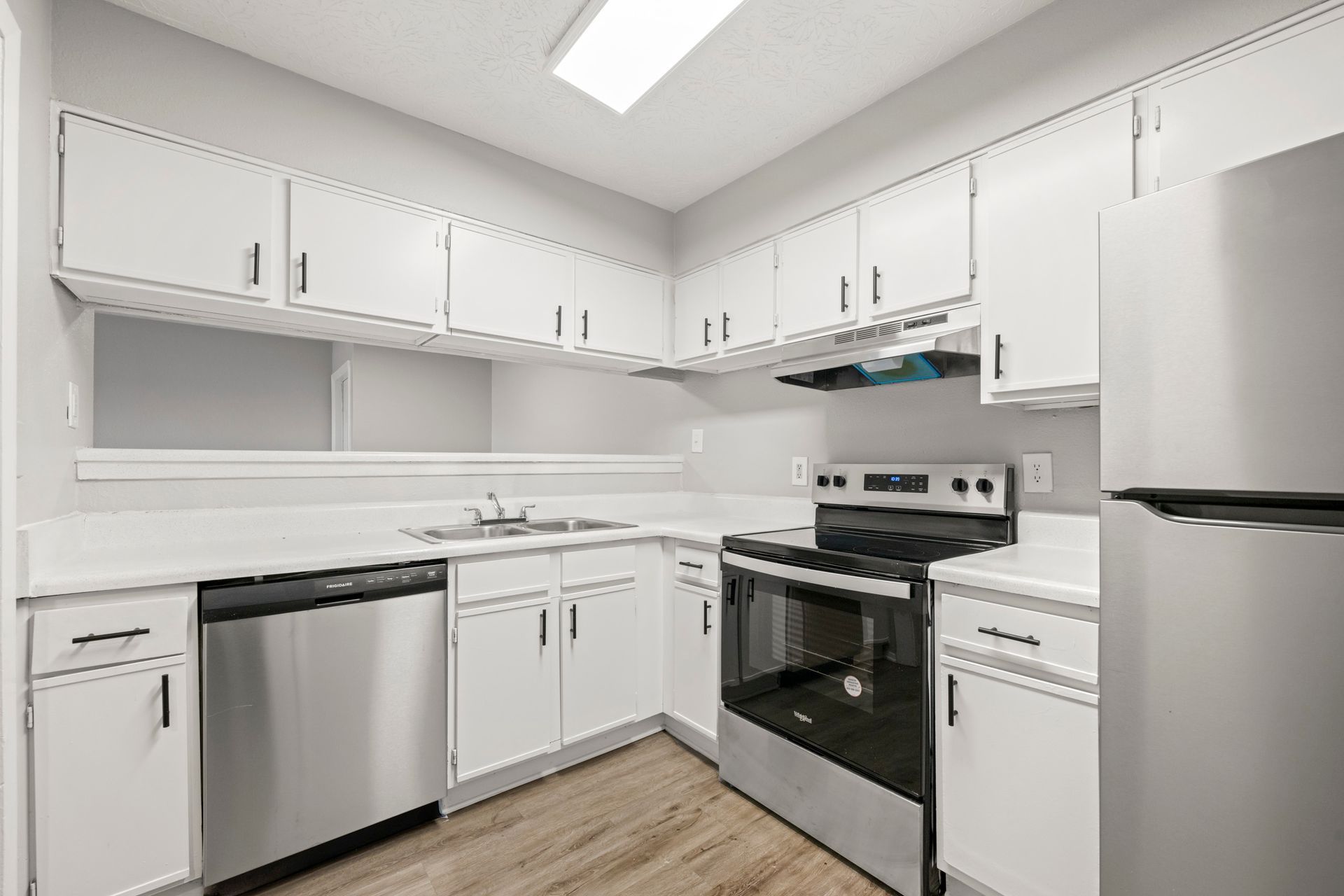 Bright white kitchen with white cabinets, stainless dishwasher, stove, and refrigerator on wood-look floor