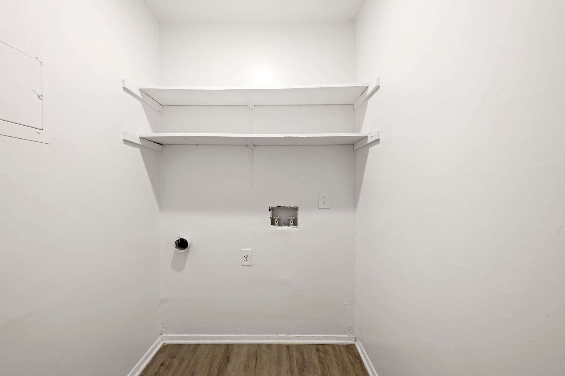 Empty white closet with two wall shelves, a hanging rod, and wood-look flooring