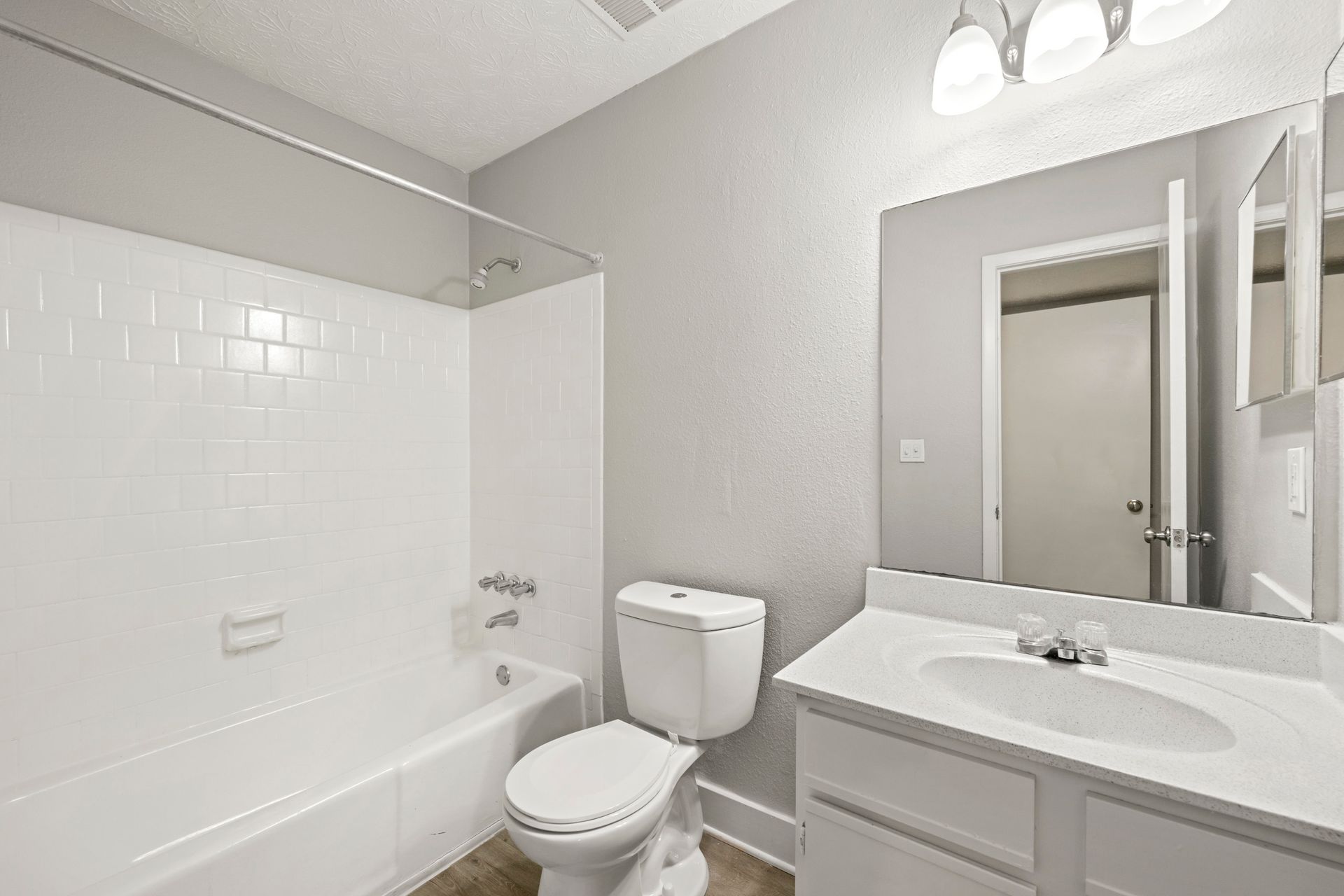 Bright white bathroom with a tub-shower, toilet, and vanity mirror sink.