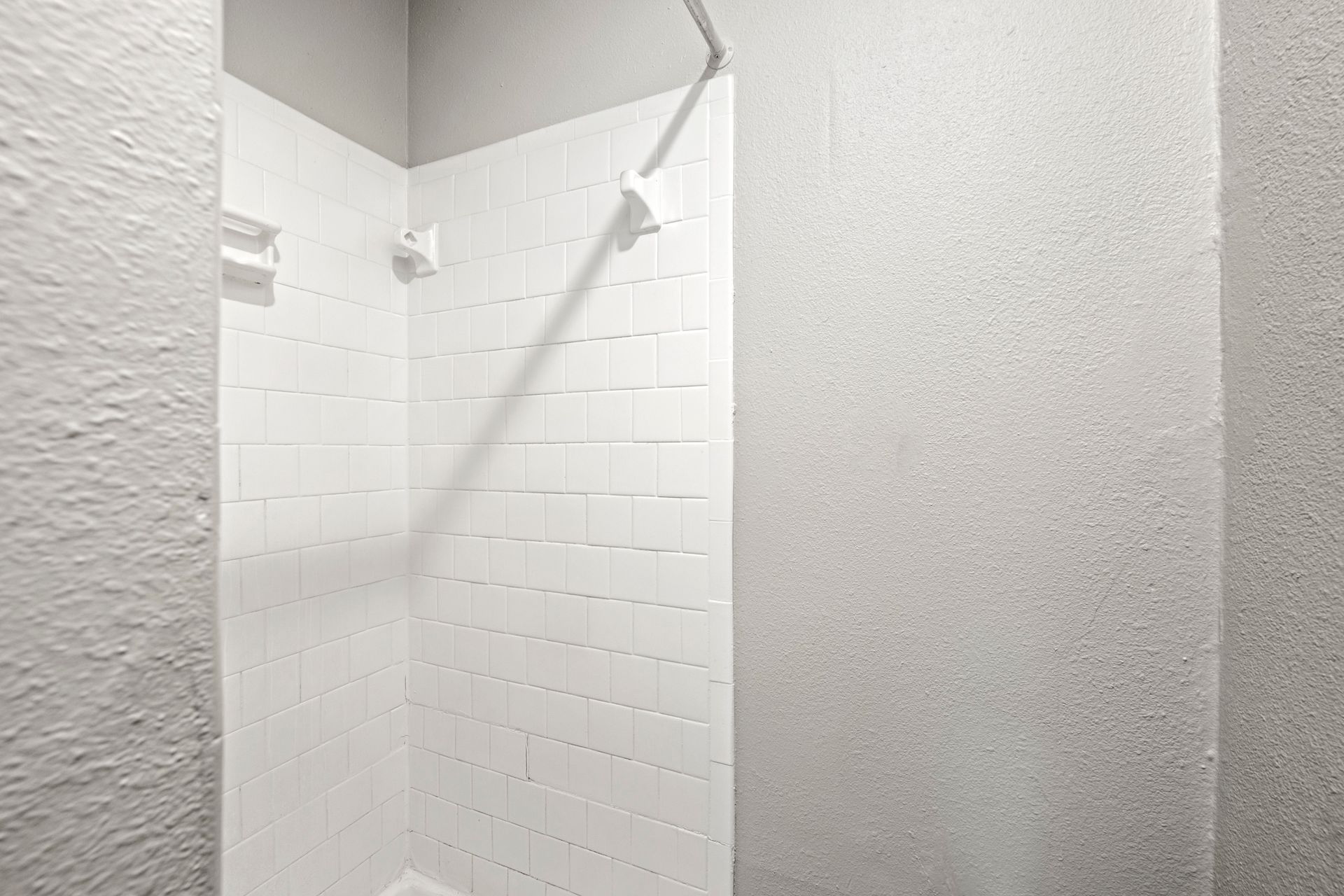 White tiled shower stall with gray walls and a slanted ceiling outdoors