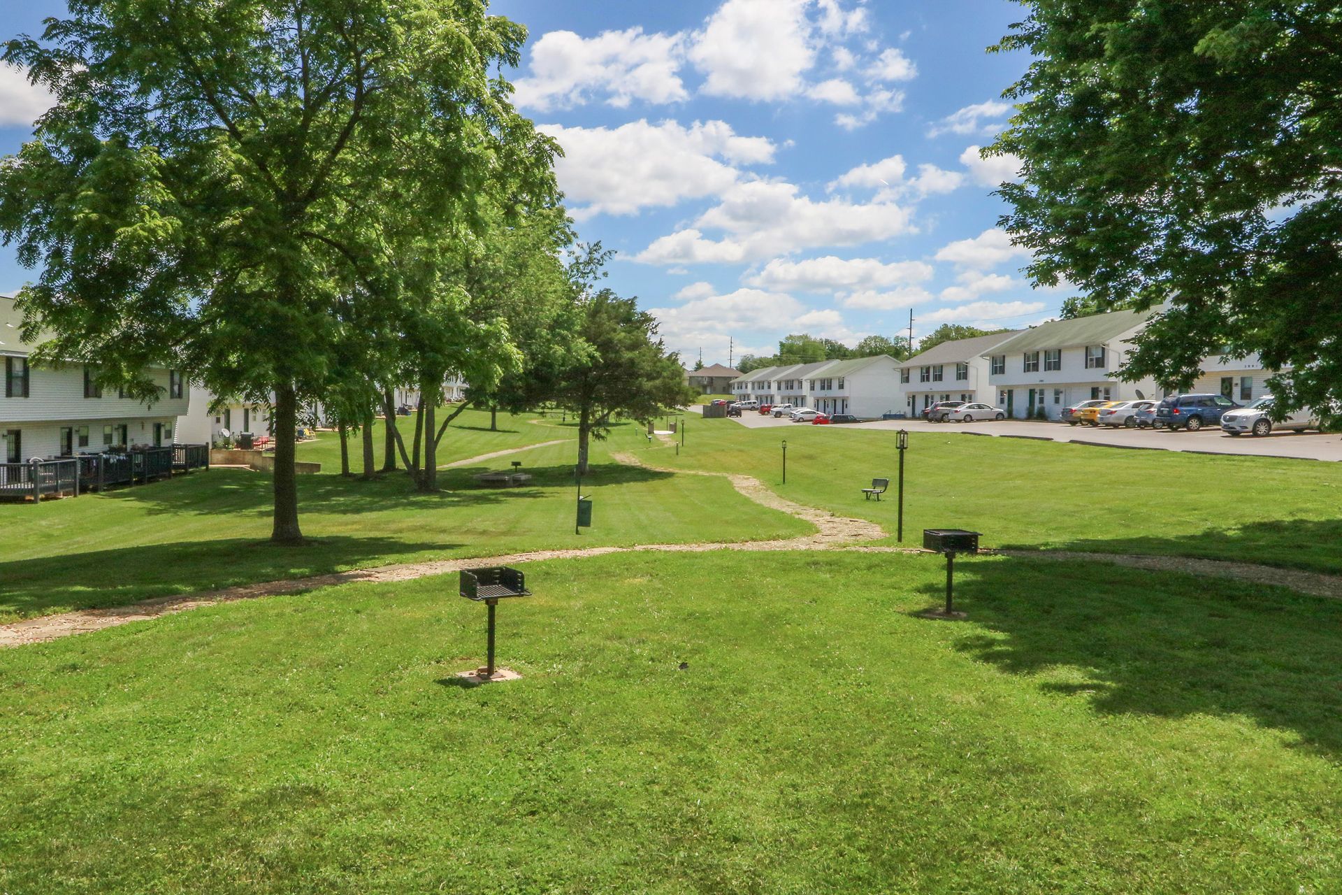 A large lush green field with trees and buildings in the background.
