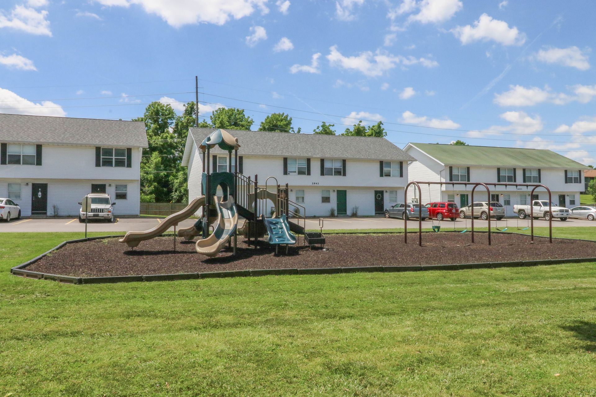 A playground with a slide and swings in front of a building.