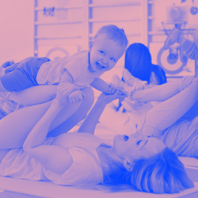 A woman is laying on a yoga mat holding a baby on her lap.