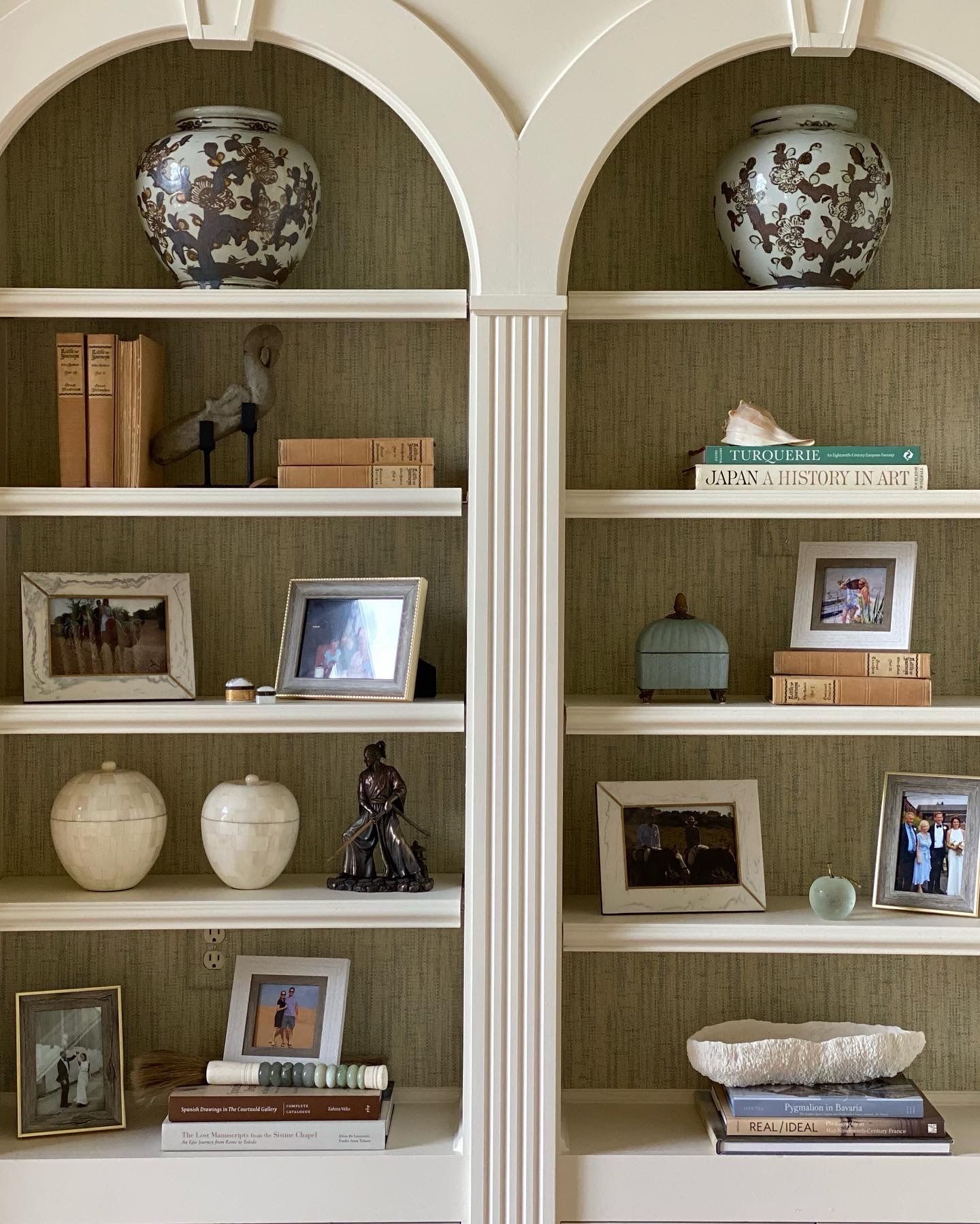 Two shelves filled with pictures vases and books