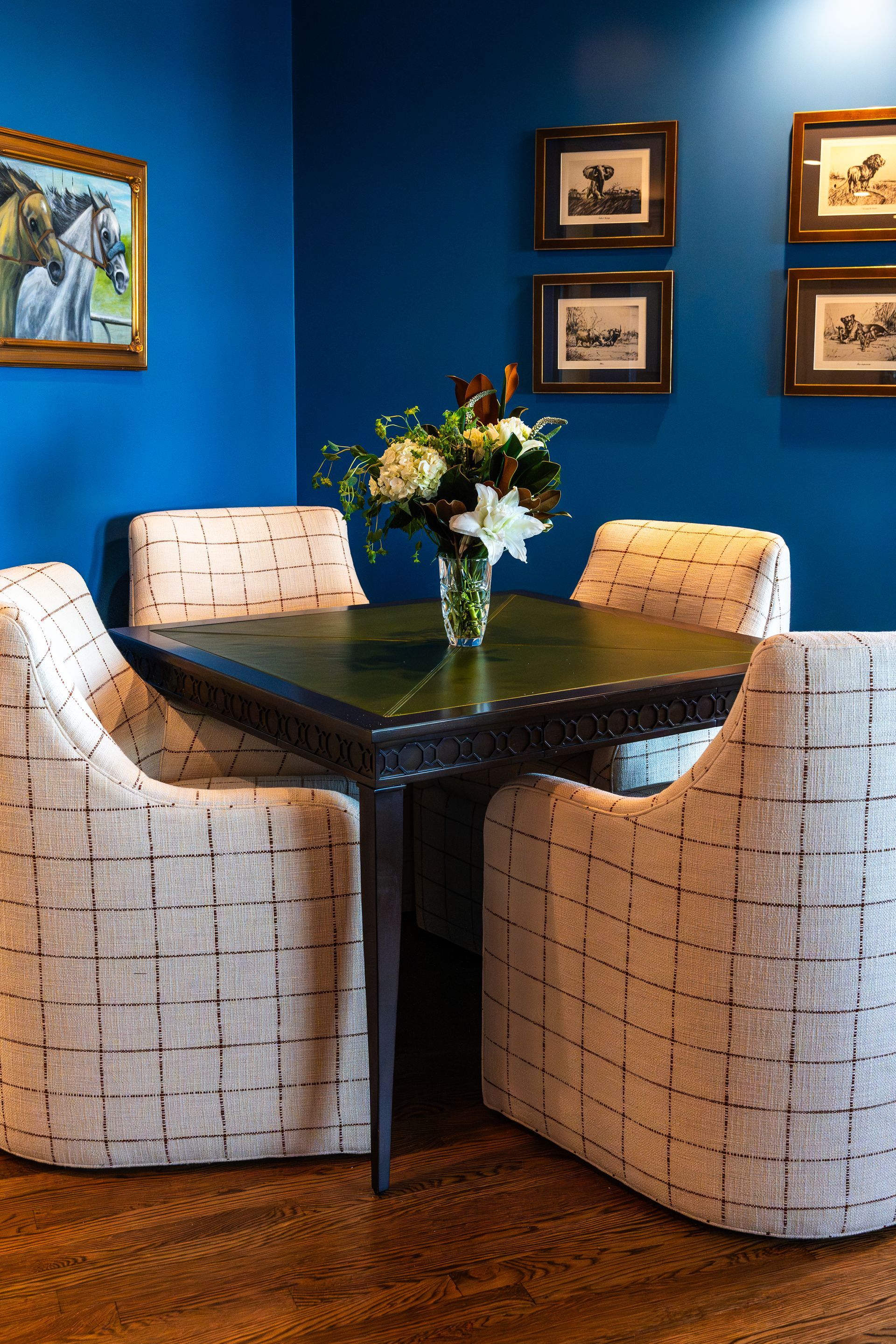A dining room with a table and chairs and a vase of flowers on it.