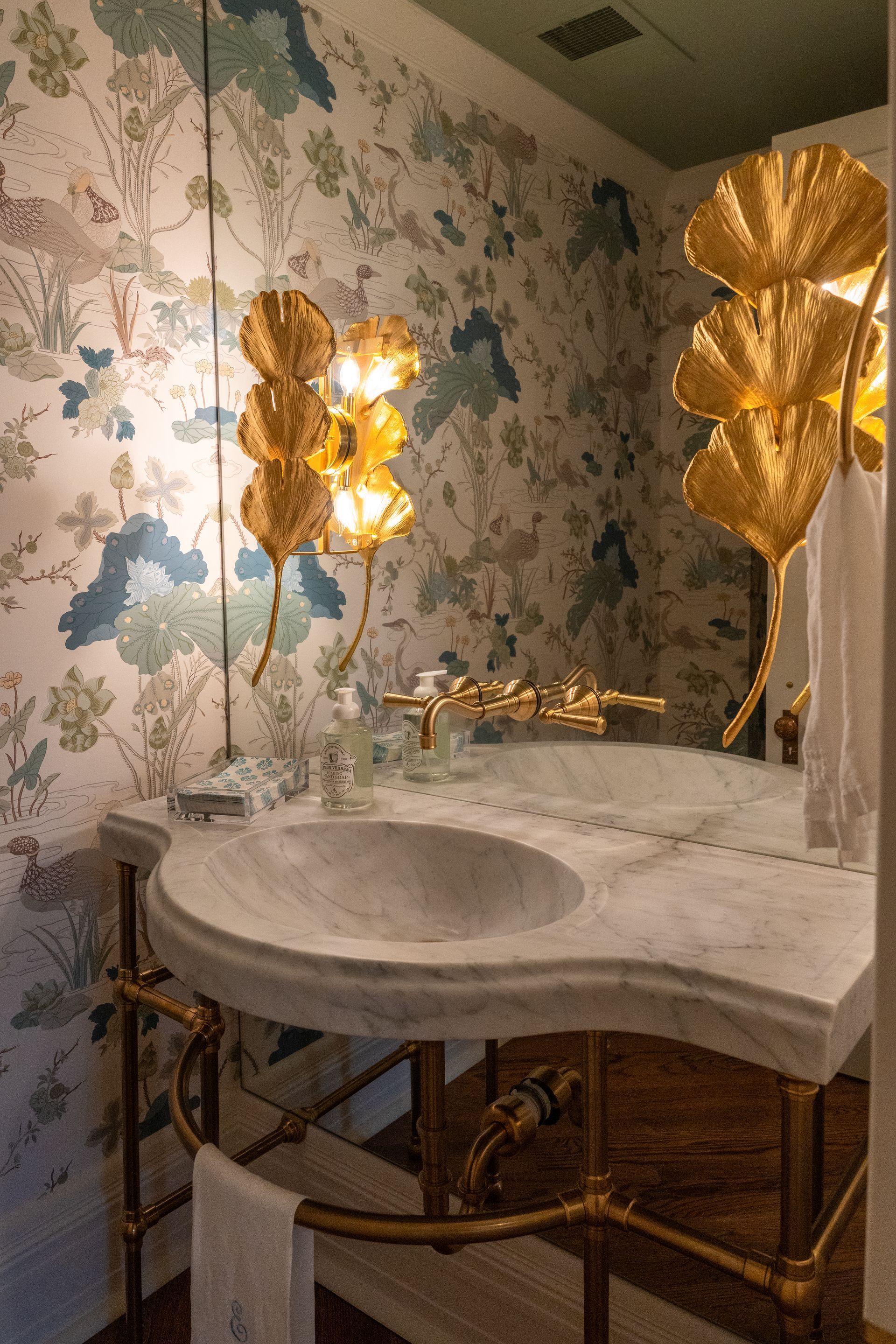 A bathroom with a sink and a mirror with gold leaves on the wall.
