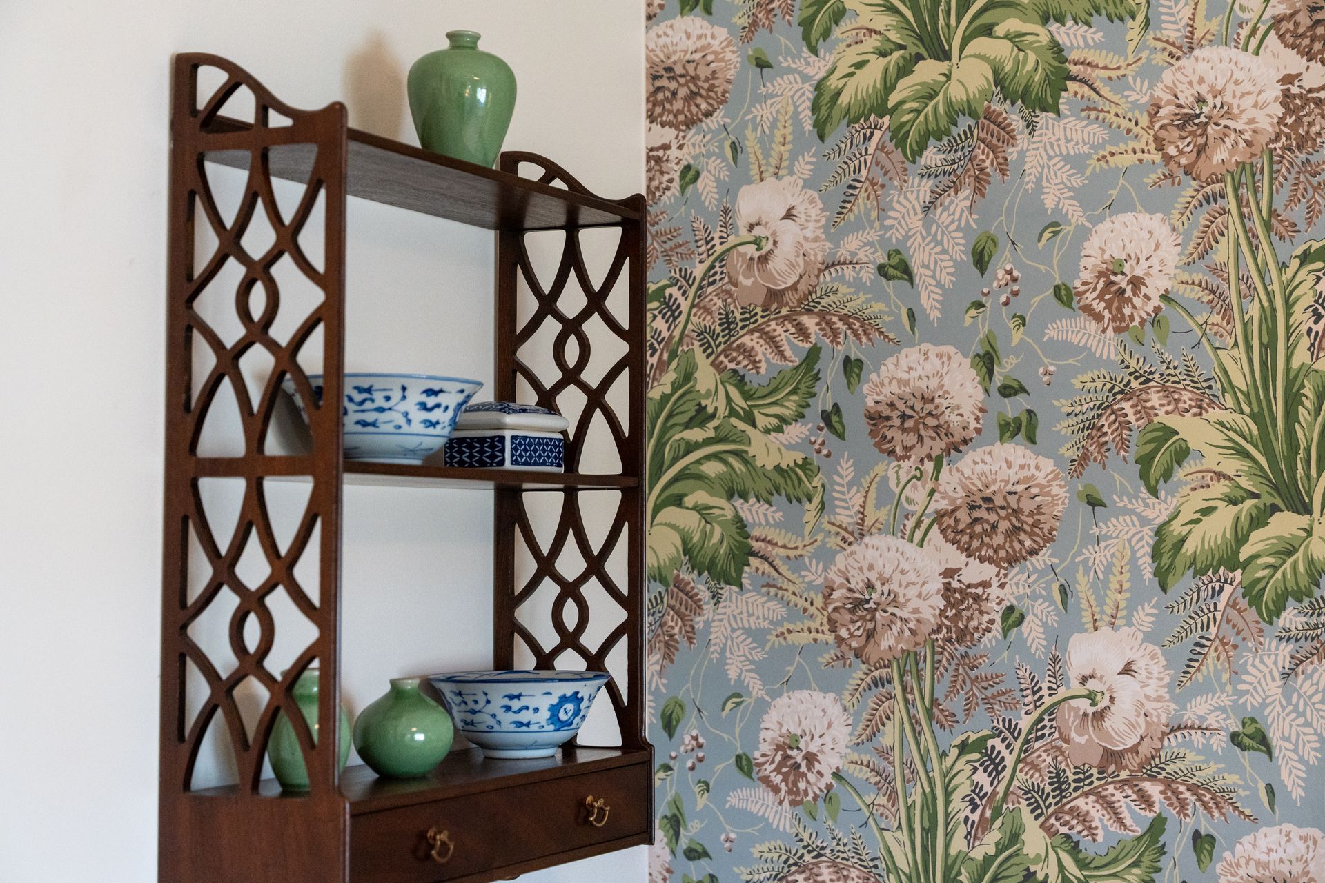 A shelf with bowls and vases on it next to a wall with floral wallpaper.
