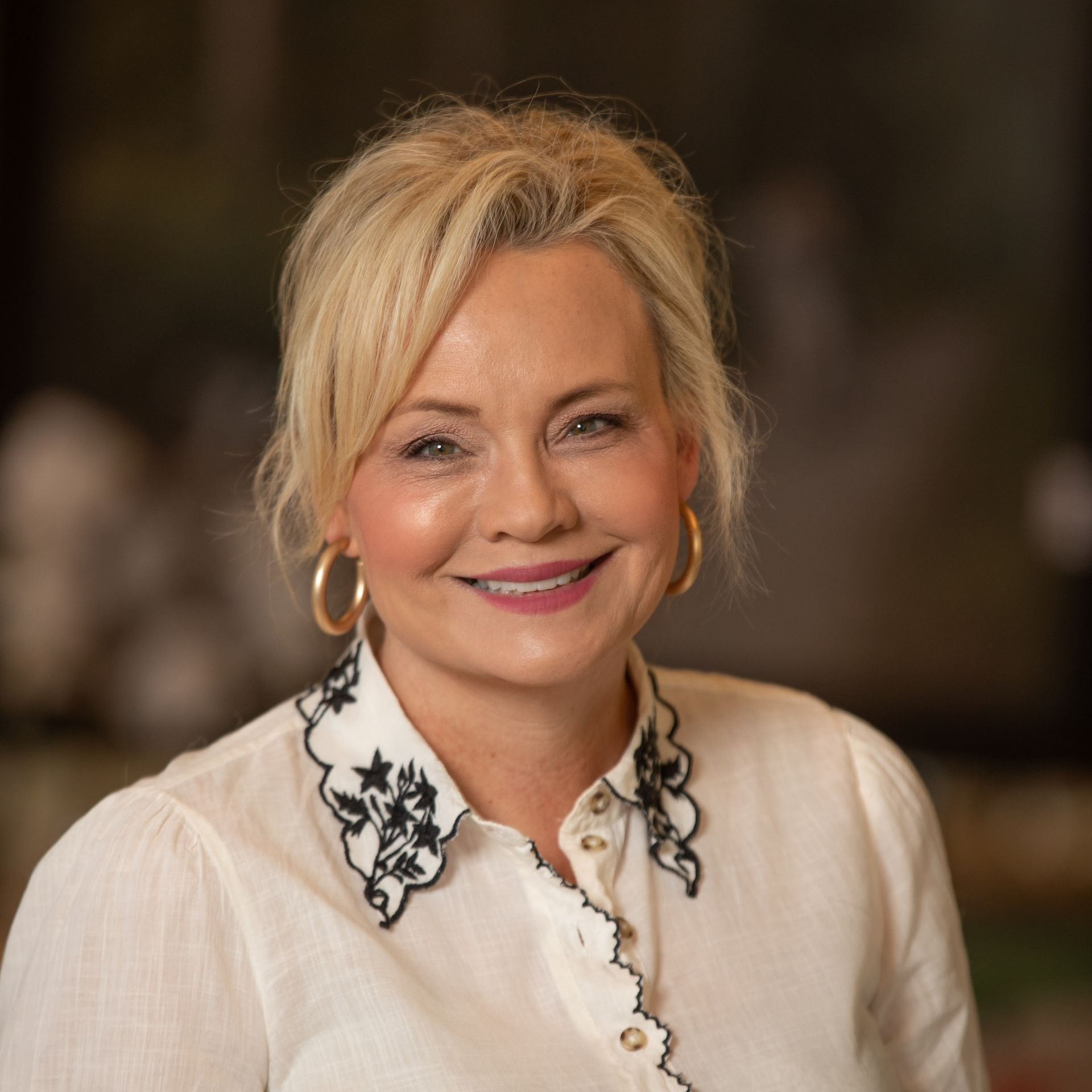 A woman wearing a white shirt with a black collar is smiling for the camera.
