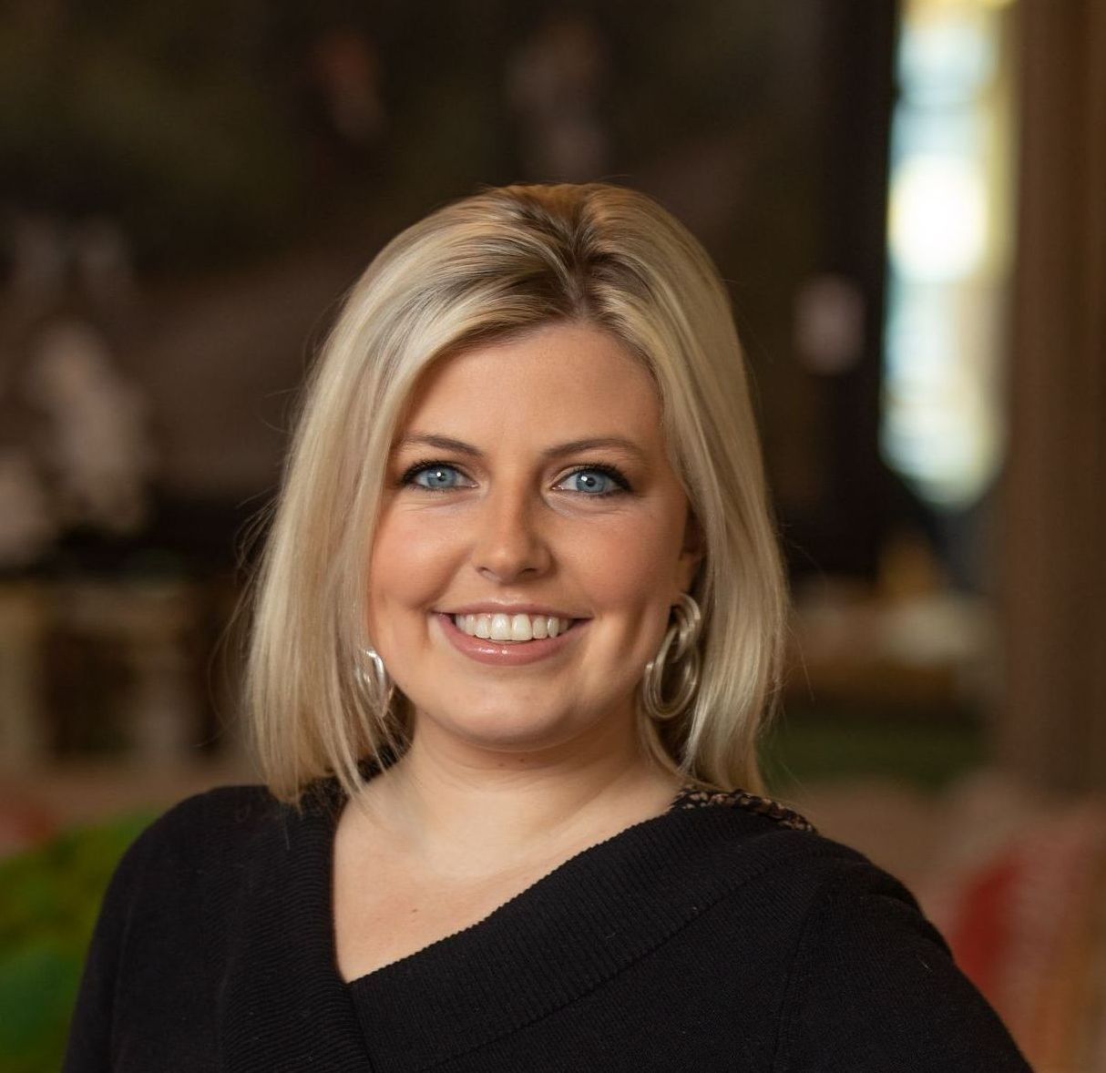 A woman wearing a black sweater and hoop earrings is smiling for the camera.