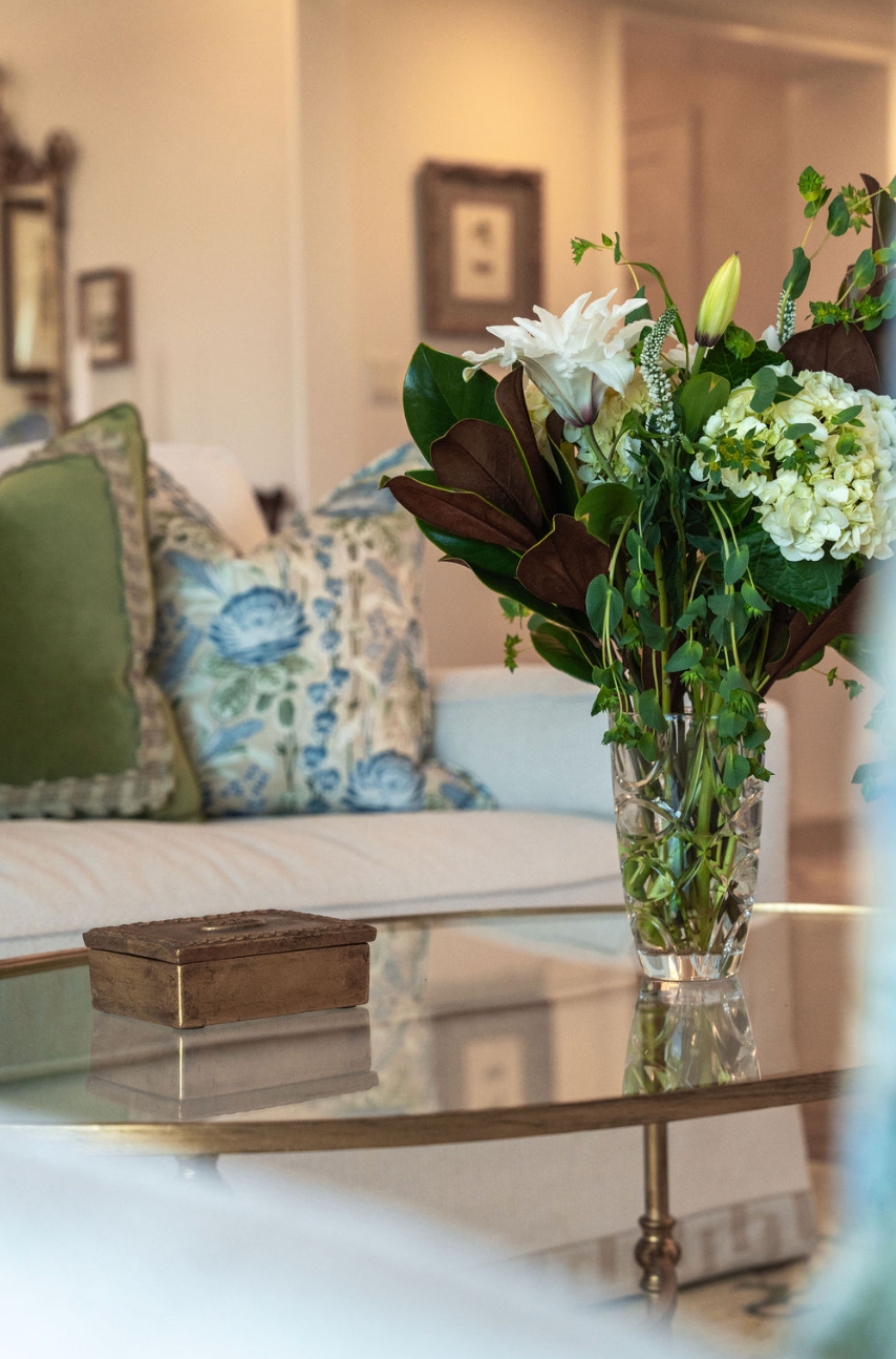 A vase of flowers is sitting on a glass coffee table in a living room.