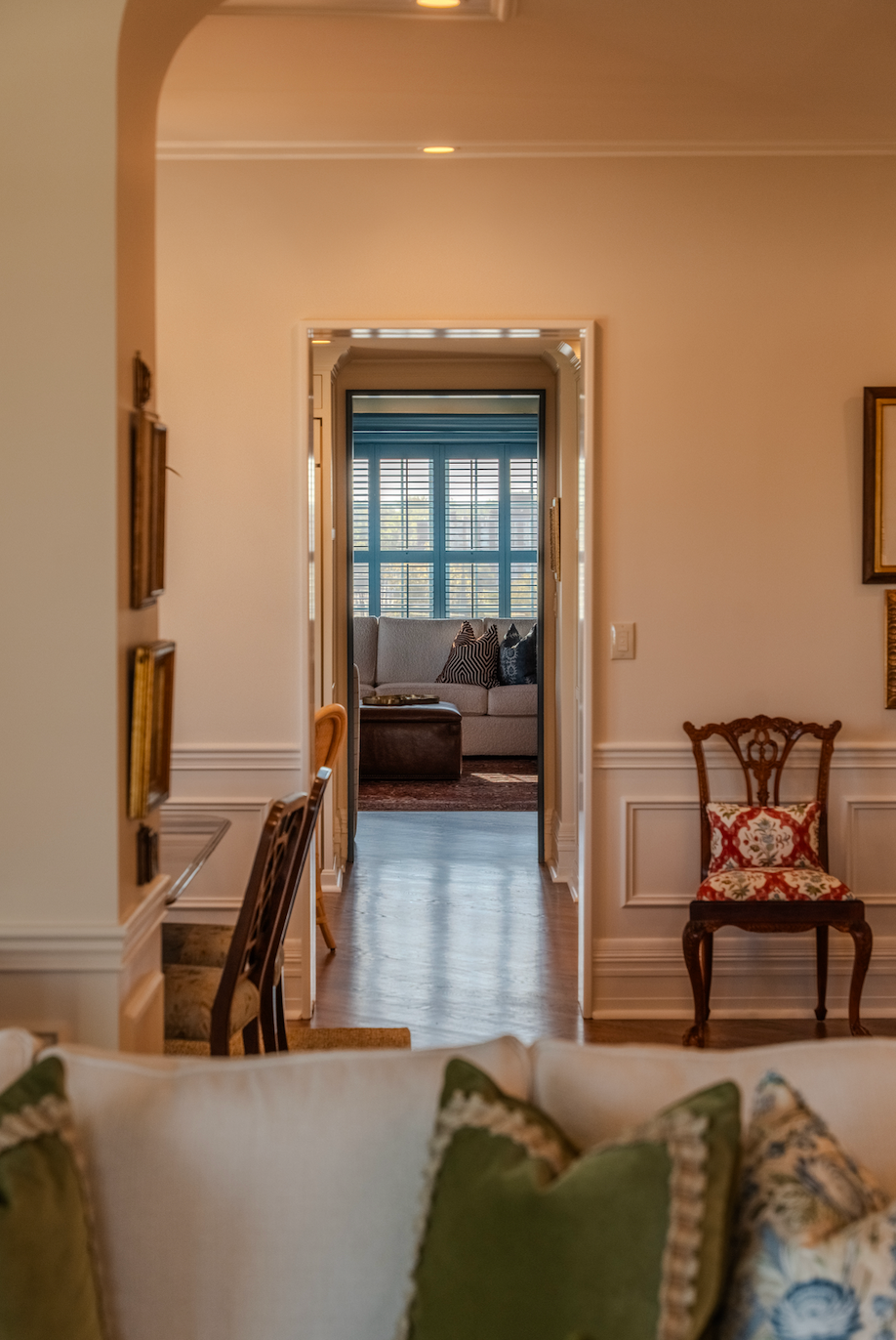 A living room with a couch and chairs and a doorway leading to a bedroom.