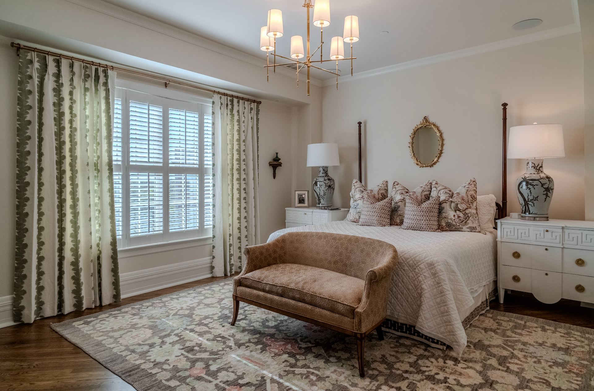 A bedroom with a large bed , a bench , lamps , curtains and a chandelier.