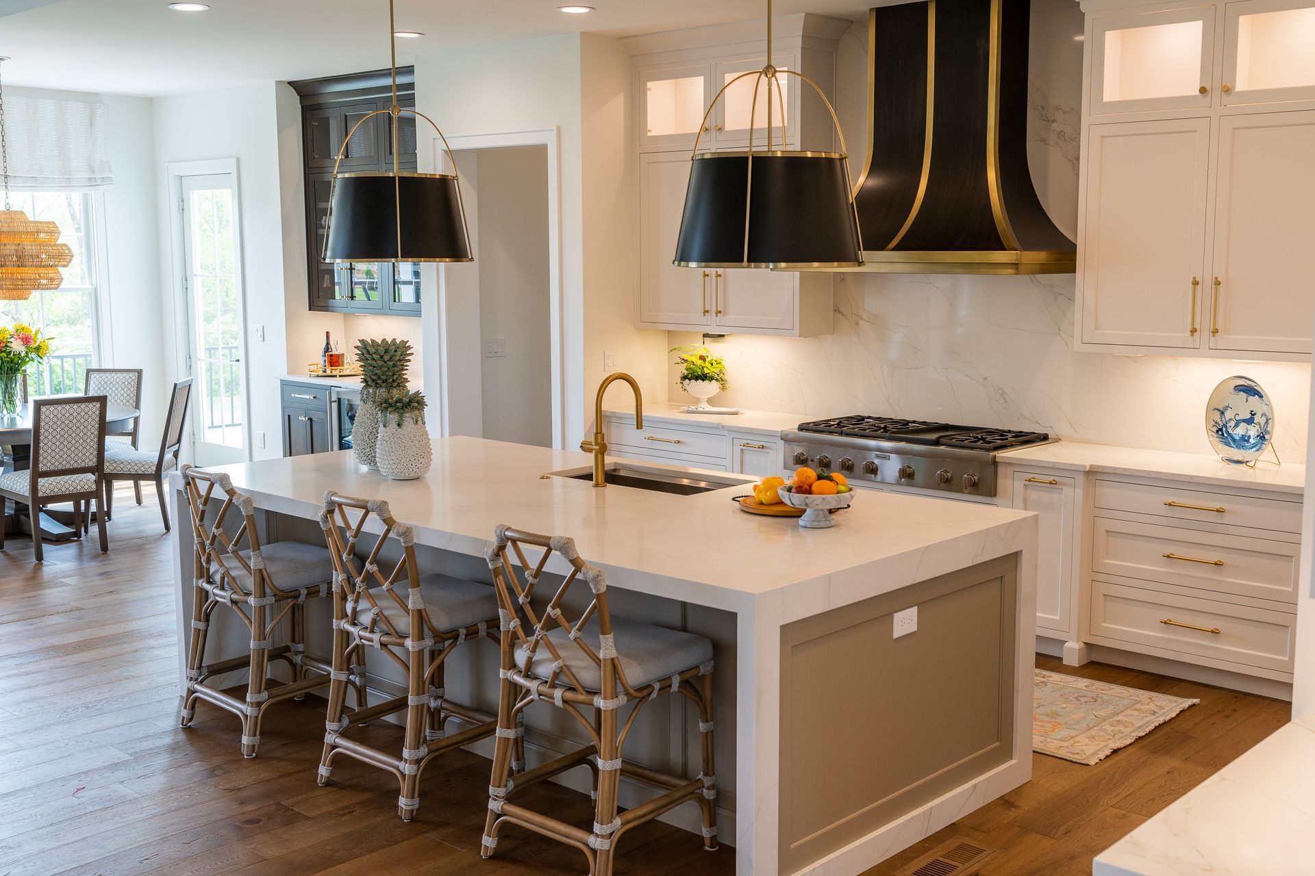 A kitchen with white cabinets , a large island , stools and a stove.