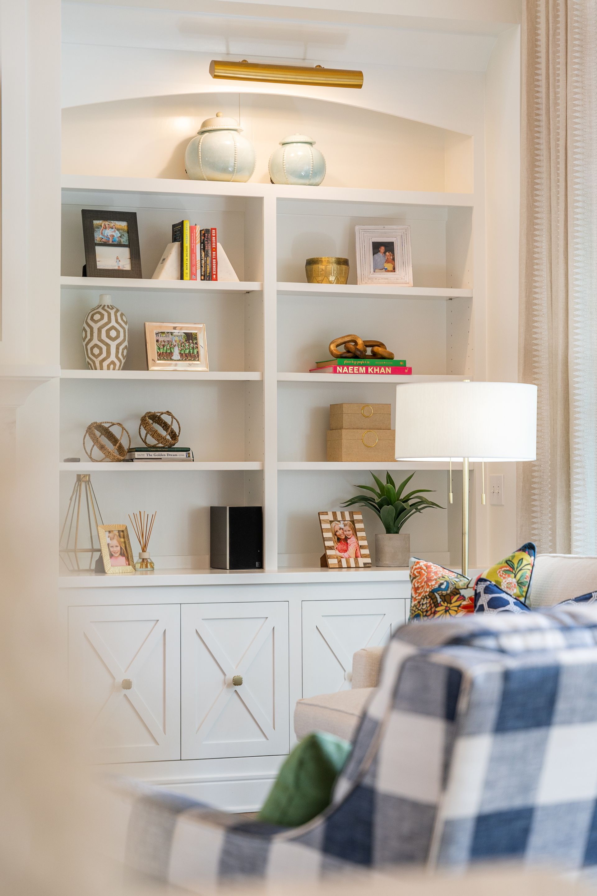 A living room with a couch , chair , bookshelf and lamp.