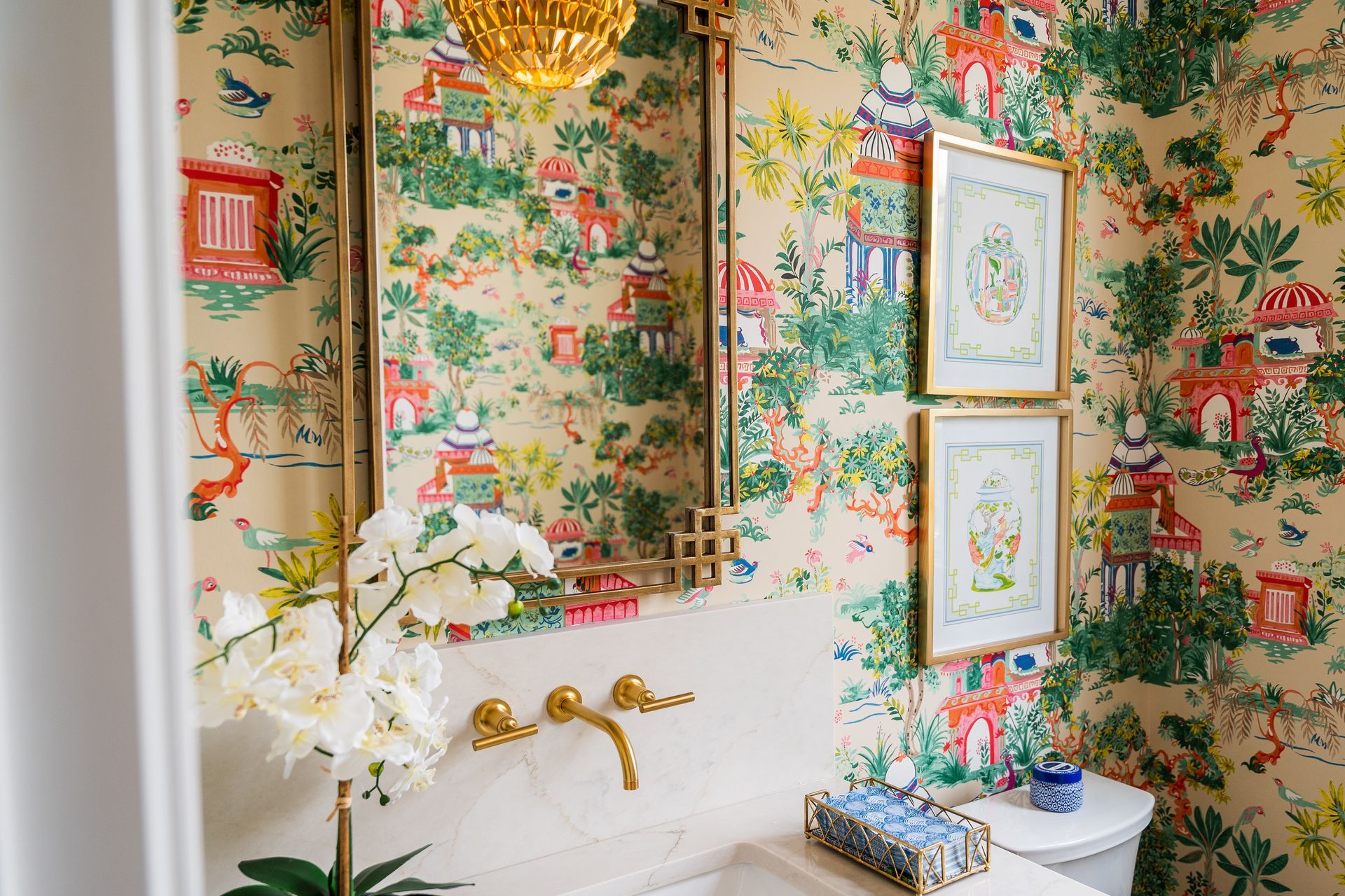 A bathroom with a sink , toilet , mirror and floral wallpaper.