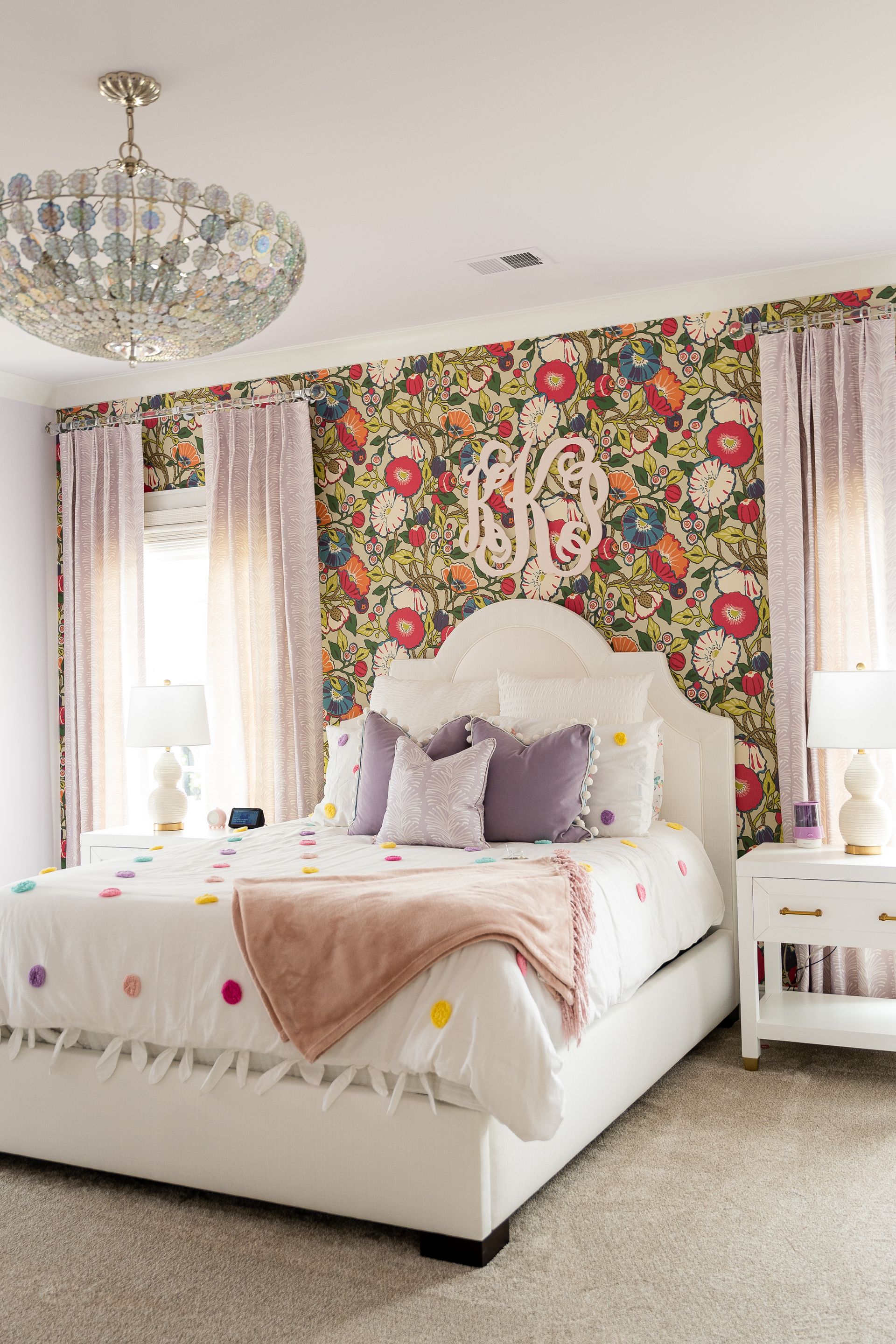 A bedroom with a bed , nightstand , chandelier and floral wallpaper.