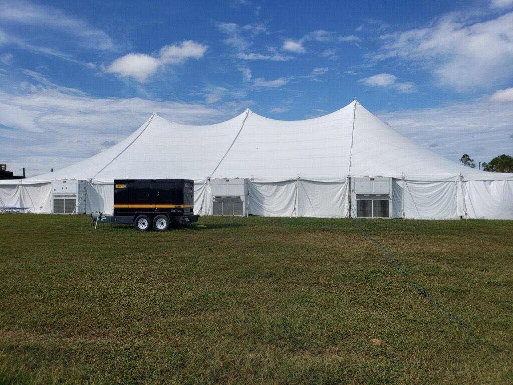 Large white event tent on green grass with a black generator trailer in front. Blue sky.
