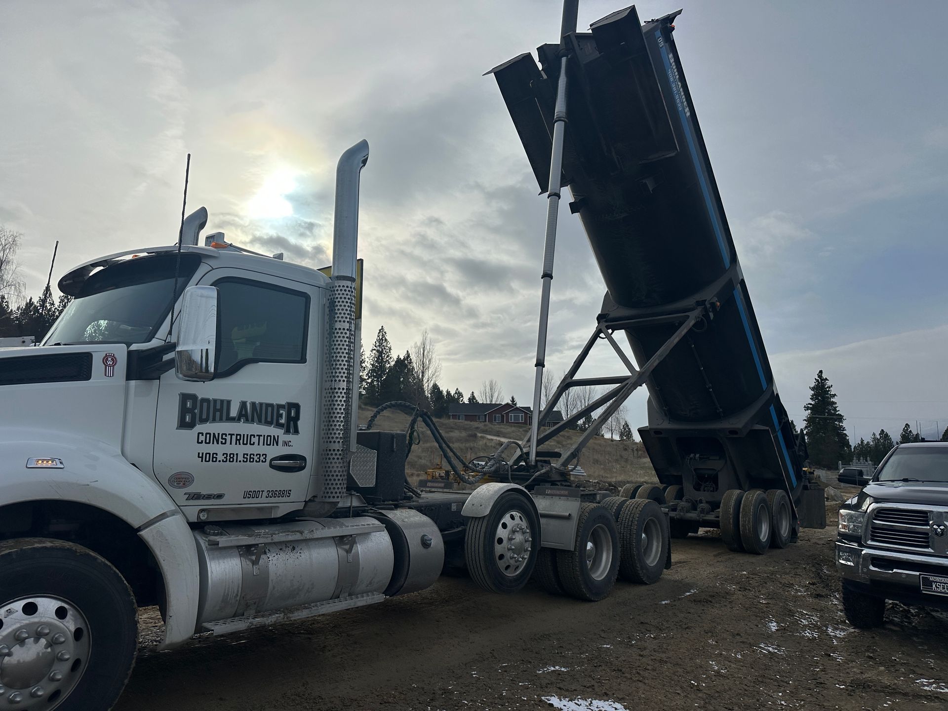 White semi-truck with raised dump trailer parked on gravel under cloudy sky.