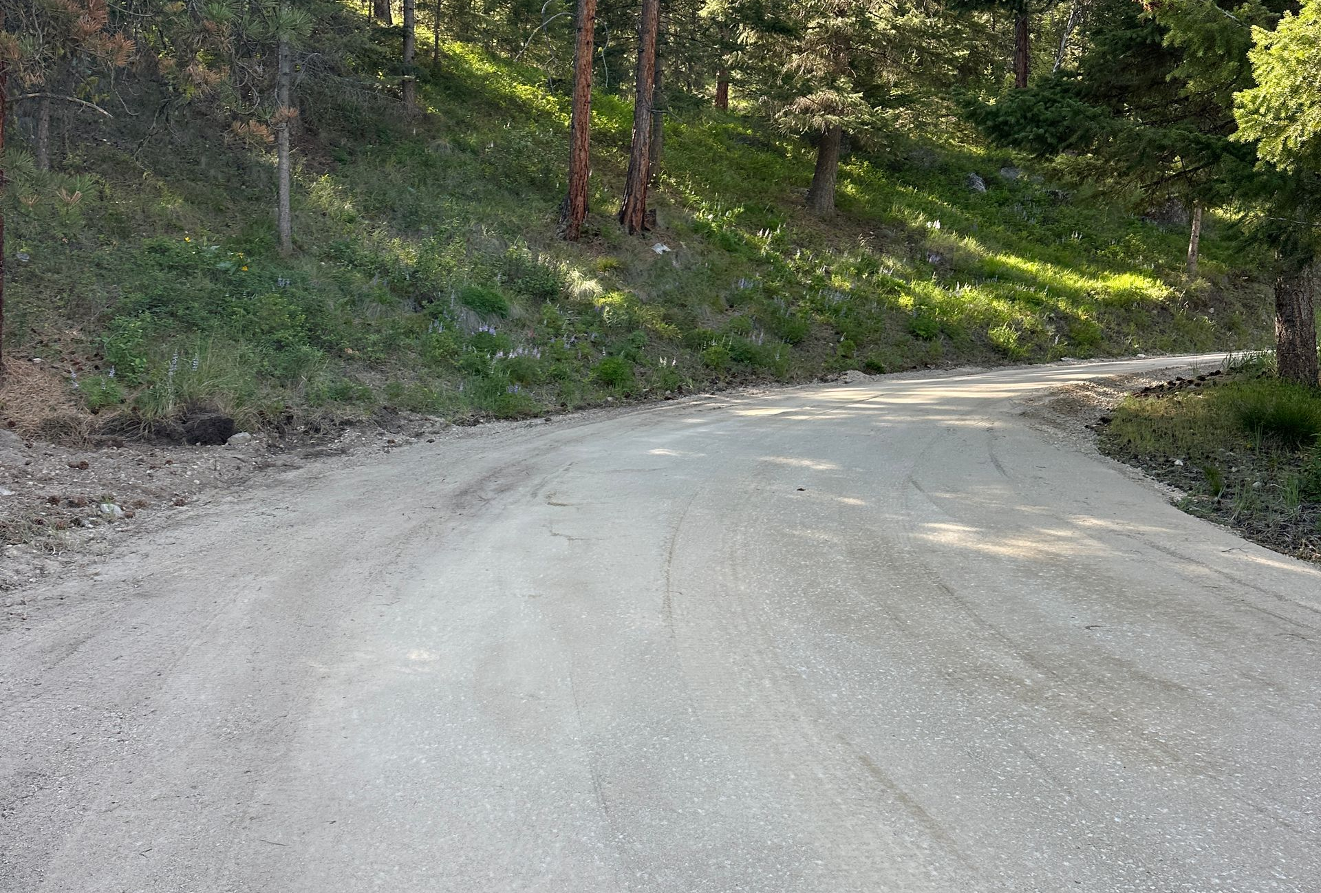 Construction site with a gravel road, rock-lined ditch, and small excavator in the distance