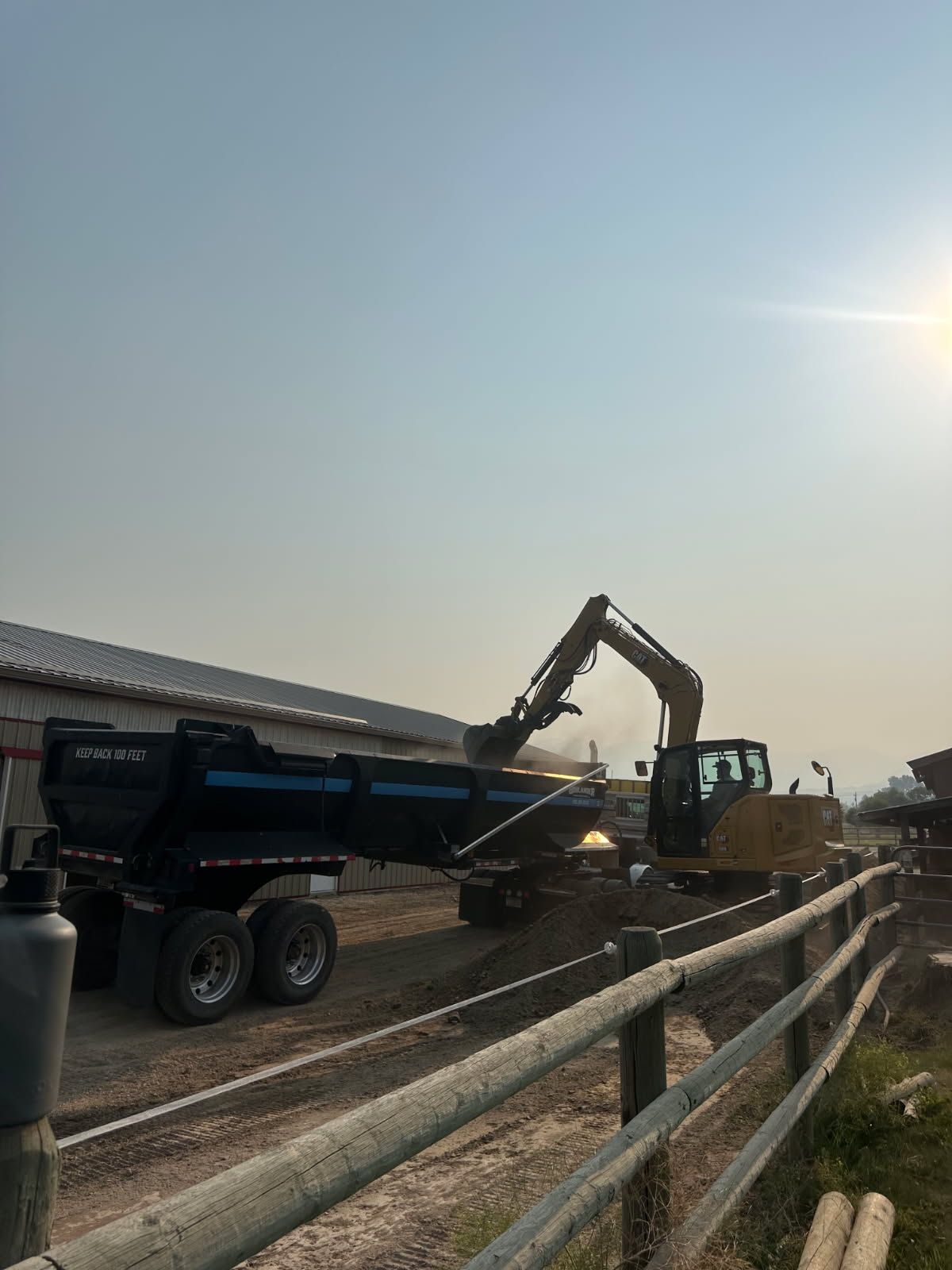 Construction dump truck unloading dirt into a conveyor by a road at sunset