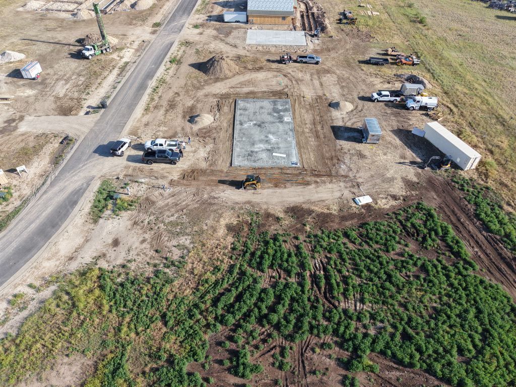 Aerial view of a road construction site with trucks, equipment, and a large concrete foundation slab.