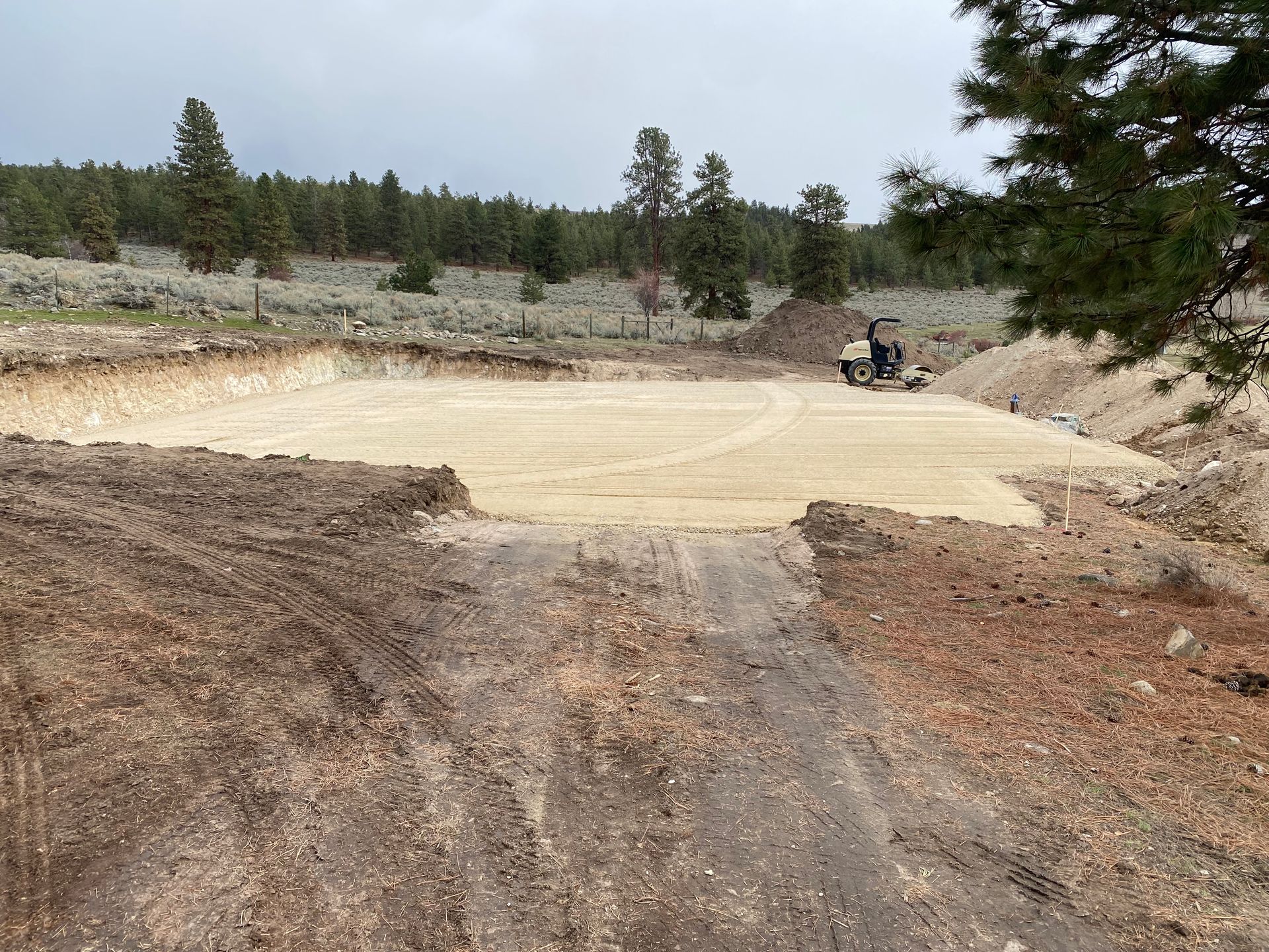 Excavated dirt pit with a small person on a motorcycle at the far side under a cloudy sky